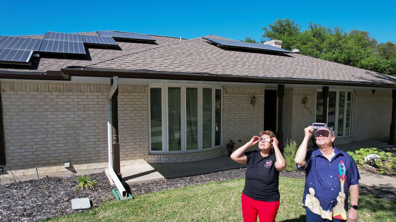 Eclipse chaser Leticia Ferrer and her husband Daniel Brookshier observe the sun through eclipse glasses, in front of their home in Dallas