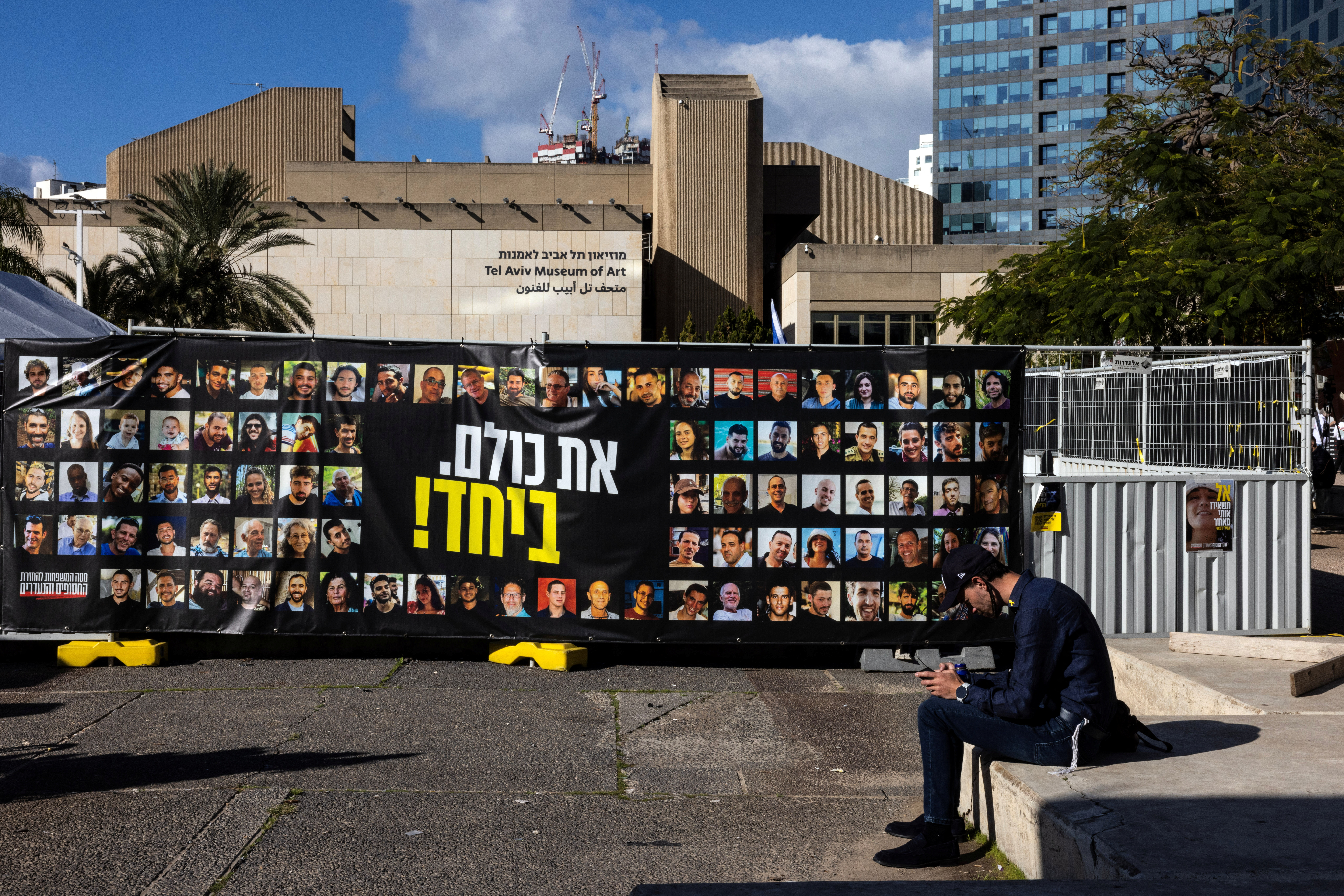 A man sits next to pictures of hostages kidnapped during the deadly October 7, 2023 attack by Hamas, in Tel Aviv