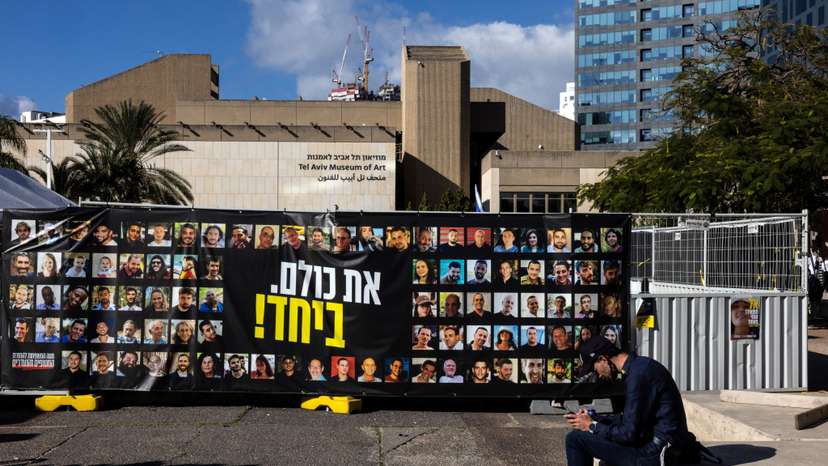A man sits next to pictures of hostages kidnapped during the deadly October 7, 2023 attack by Hamas, in Tel Aviv