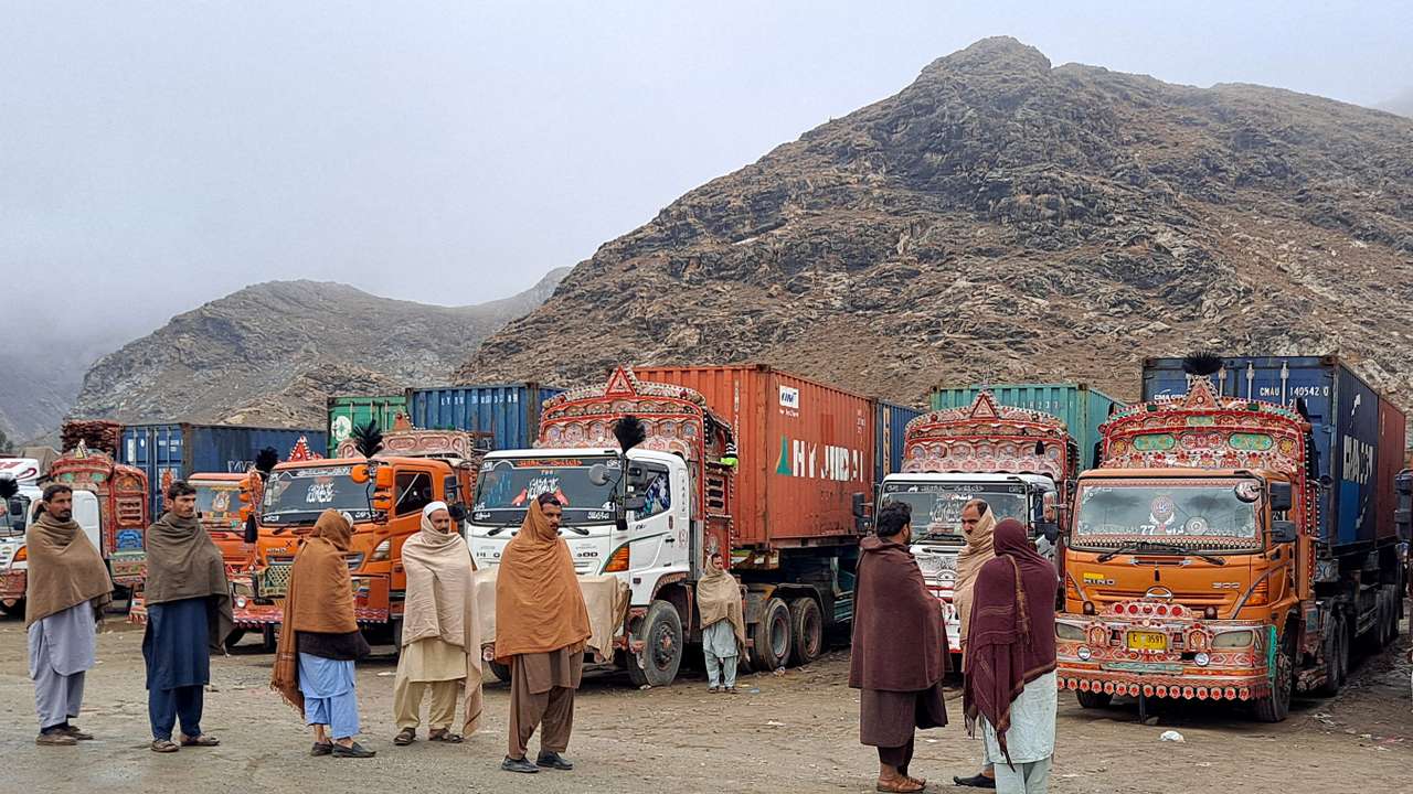 People stand next to parked trucks loaded with supplies at the Torkham border