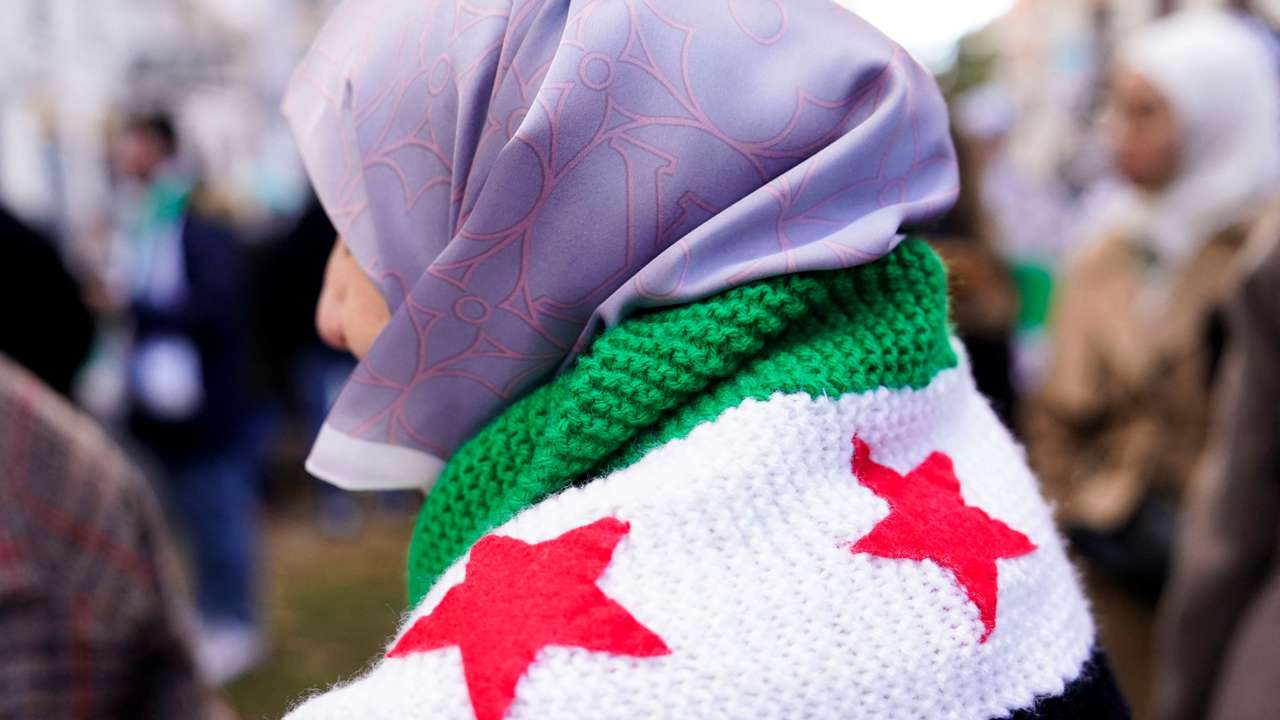 A person wears a crocheted Syrian opposition flag during a demonstration celebrating the fall of Bashar Al-Assad regime outside the Syrian embassy in Madrid