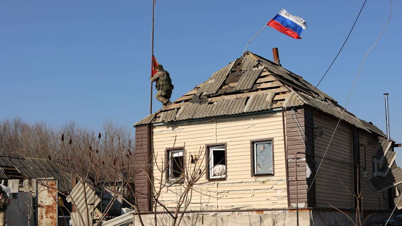 A Russian service member places a flag oh the roof of a house in Kursk region
