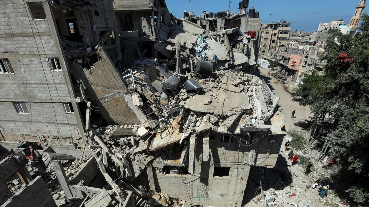 Palestinians walk past a house hit in an Israeli strike, amid the Israel-Hamas conflict, in Bureij refugee camp, in the central Gaza Strip