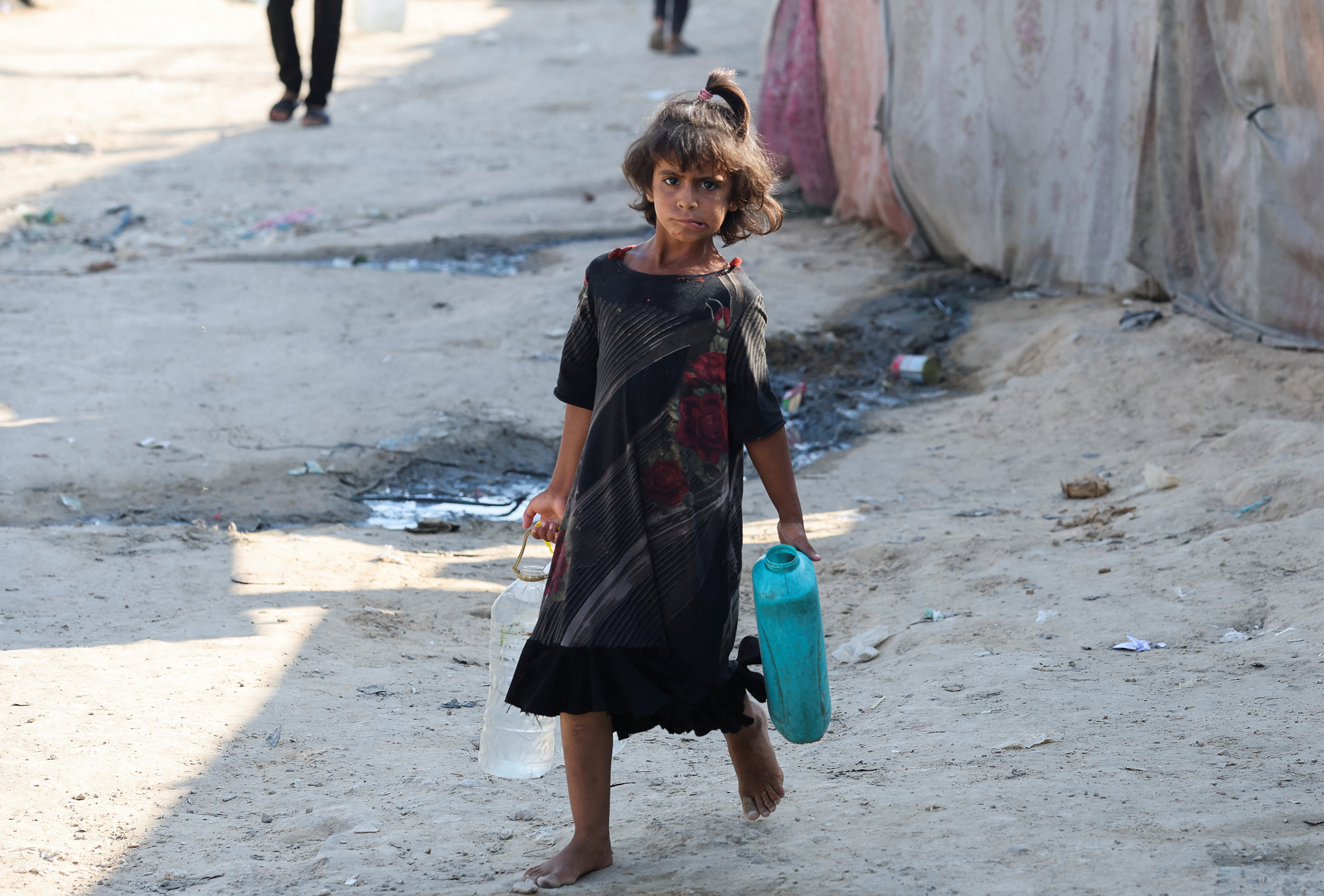 Palestinians carry containers to fill them with water, amid the Israel-Hamas conflict, in Deir Al-Balah