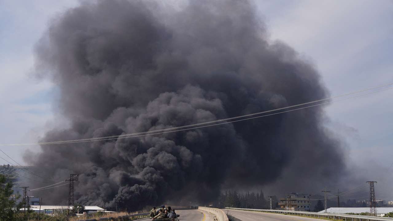 Smoke rises while members of the Syrian forces ride on a vehicle in Latakia