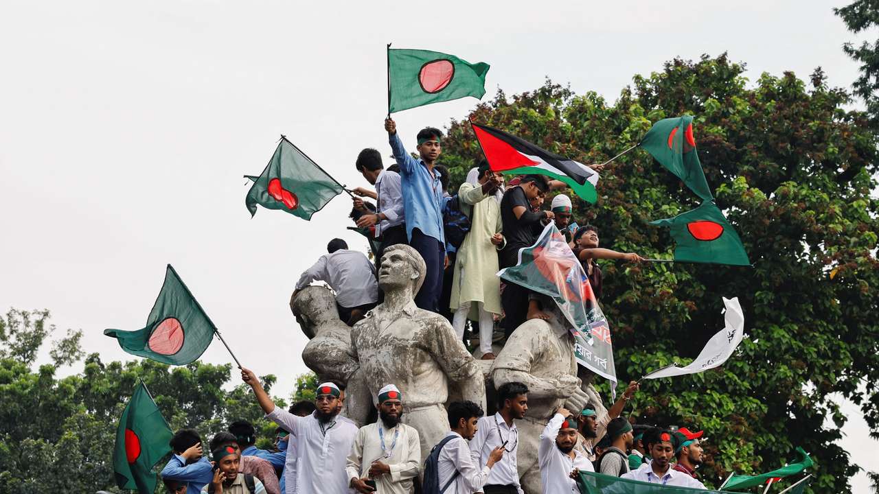 Students against discrimination wave flags by standing on top of Raju Memorial Sculpture, in Dhaka