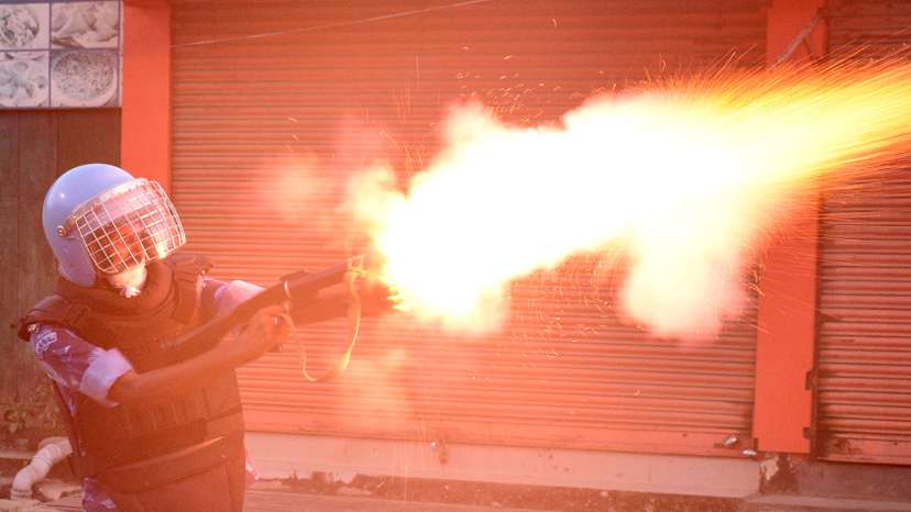 A riot police officer fires a tear smoke shell to disperse demonstrators, in Imphal