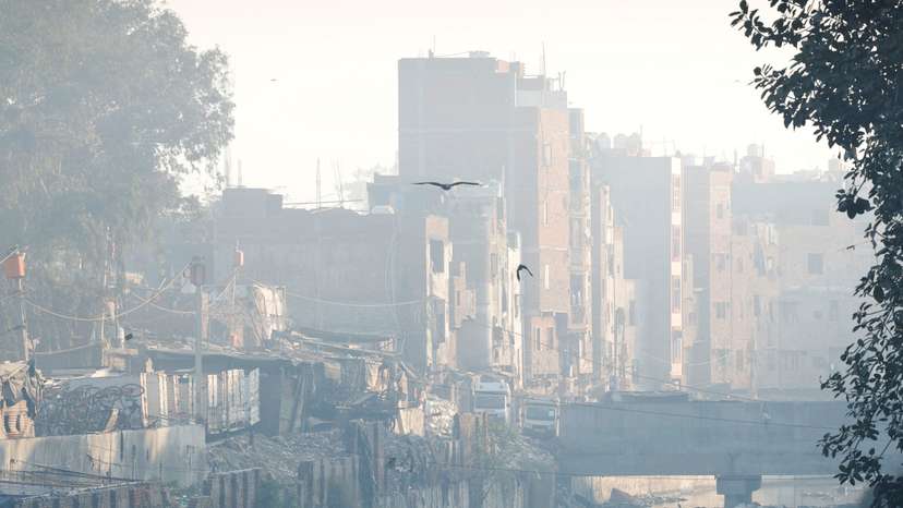 A man walks on a footbridge across an open drainage channel as the sky is enveloped in smog, in New Delhi