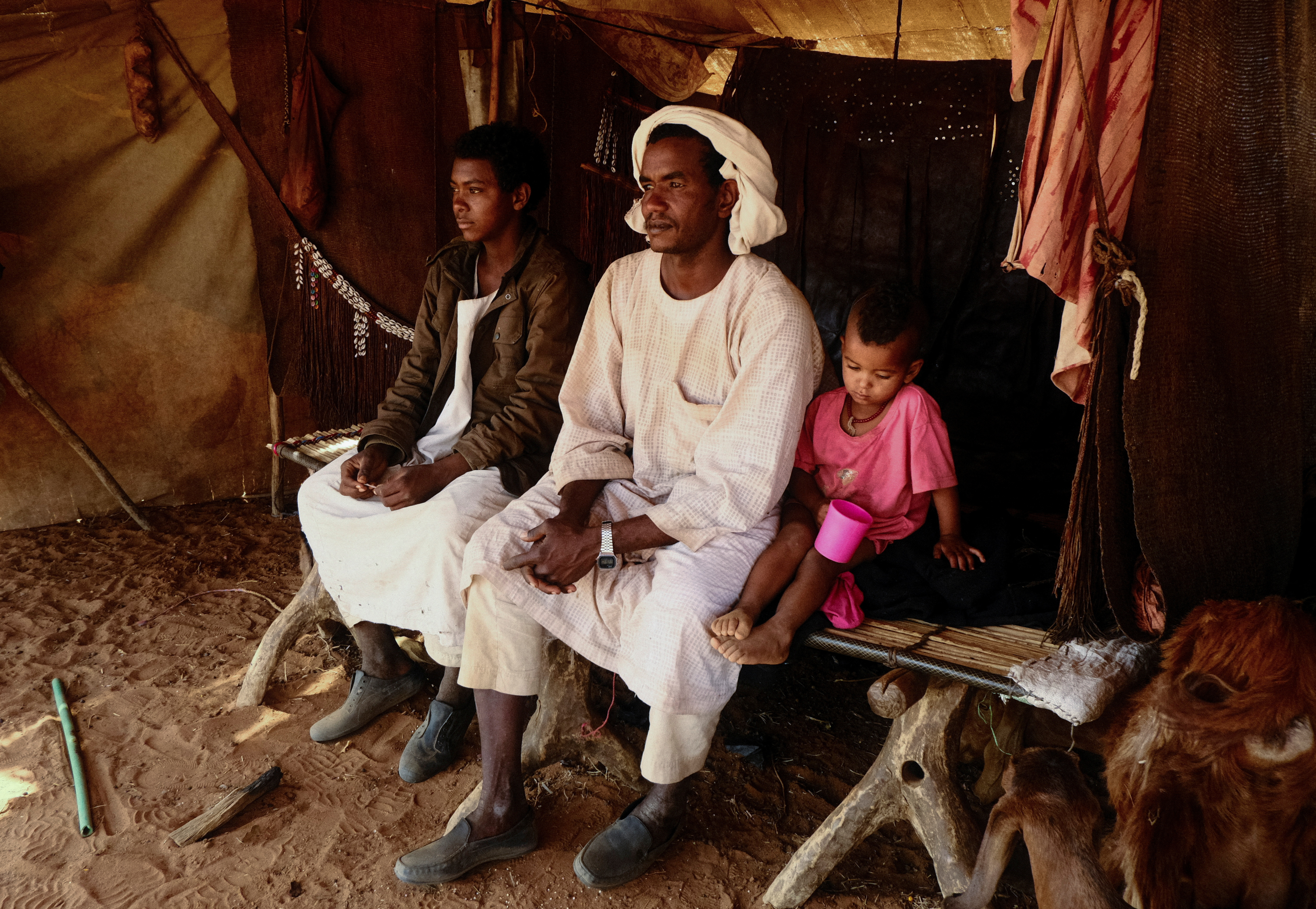 Nomadic herders sitting on a bed made of tree trunks inside their tent, North Kordofan