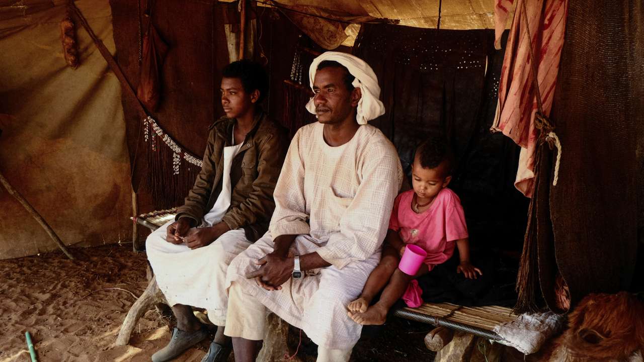 Nomadic herders sitting on a bed made of tree trunks inside their tent, North Kordofan