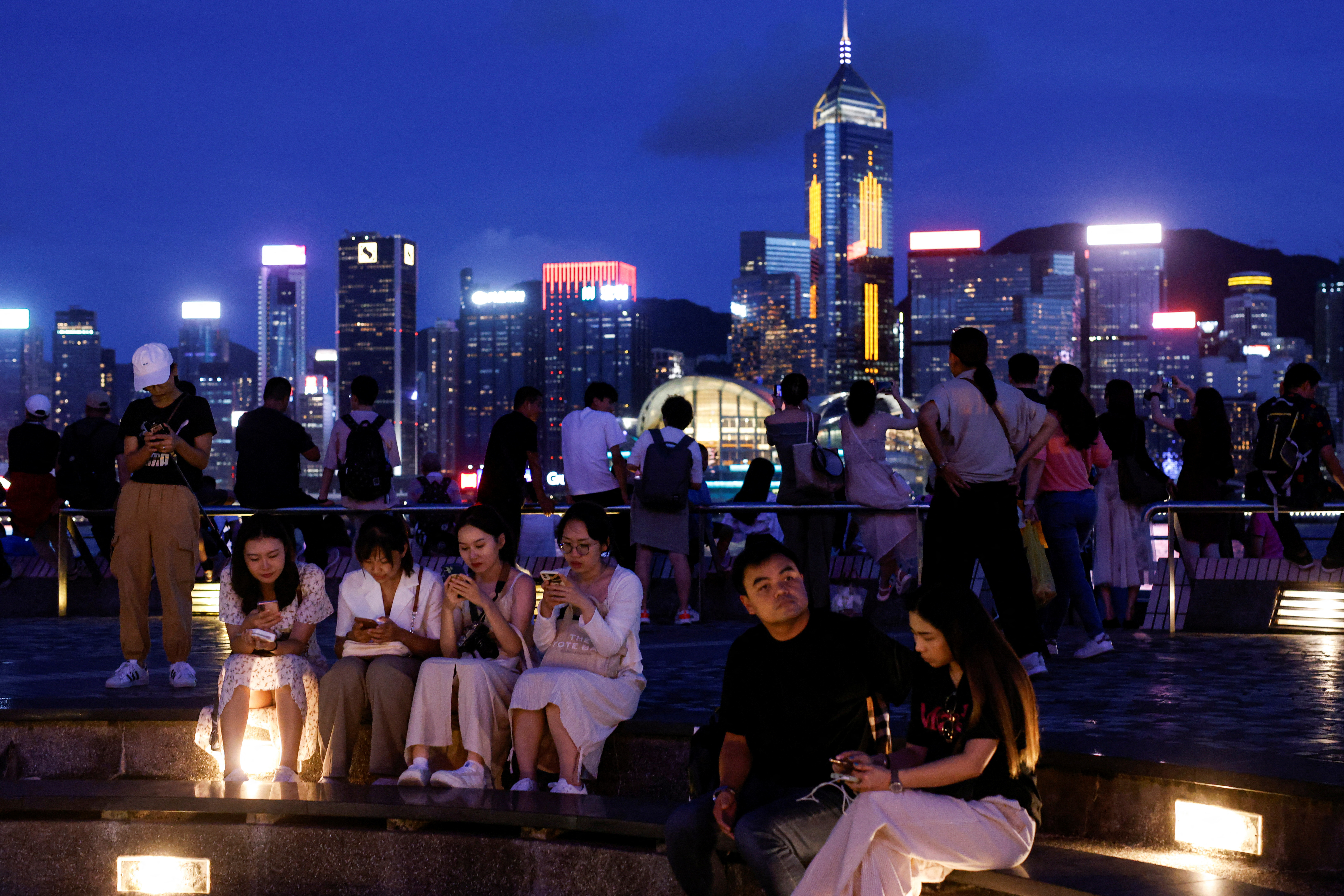 FILE PHOTO: Tourists relax on the waterfront in front of Victoria Harbour, in Hong Kong