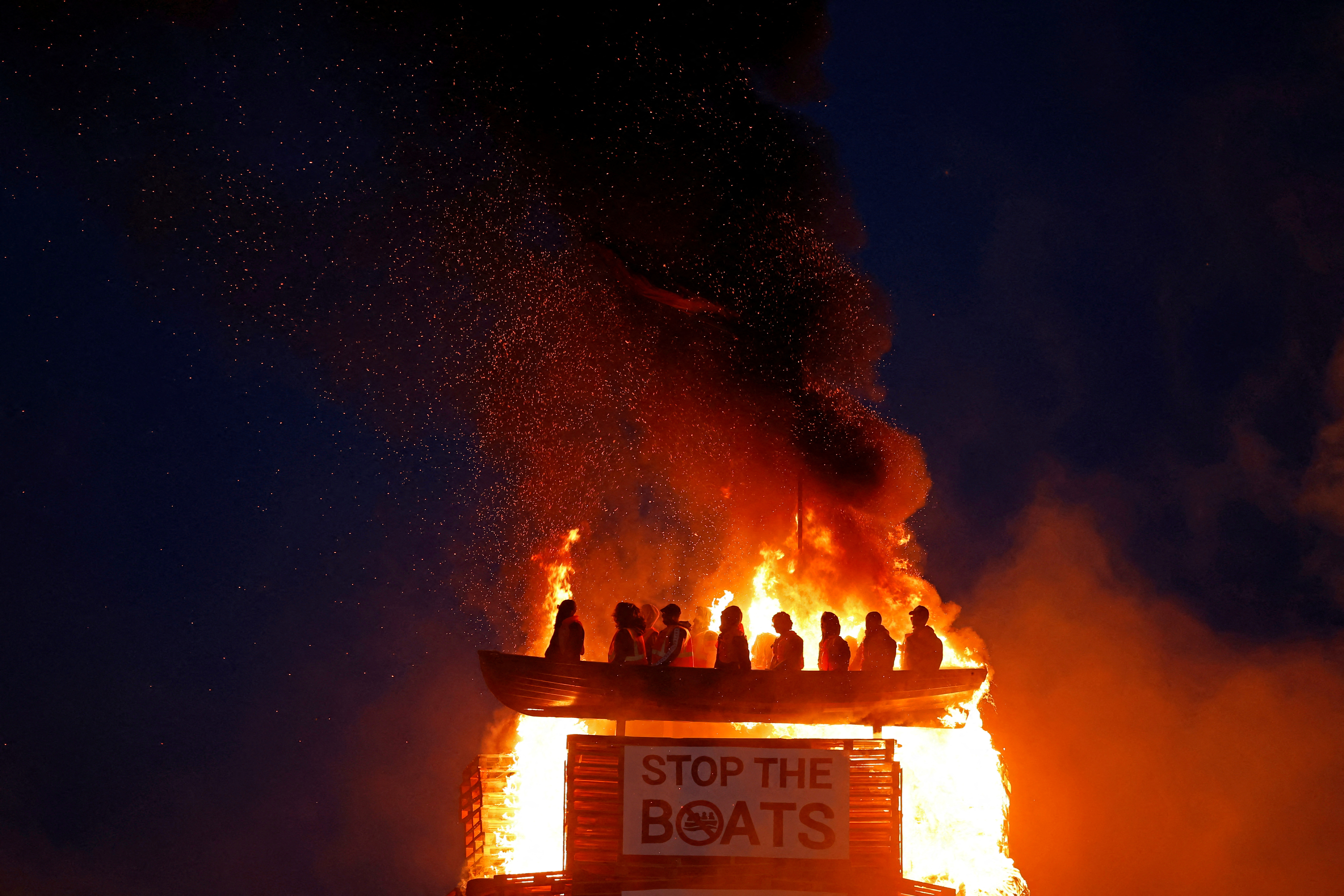 Bonfire burns with effigy of migrants in a boat atop it, in Moygashel