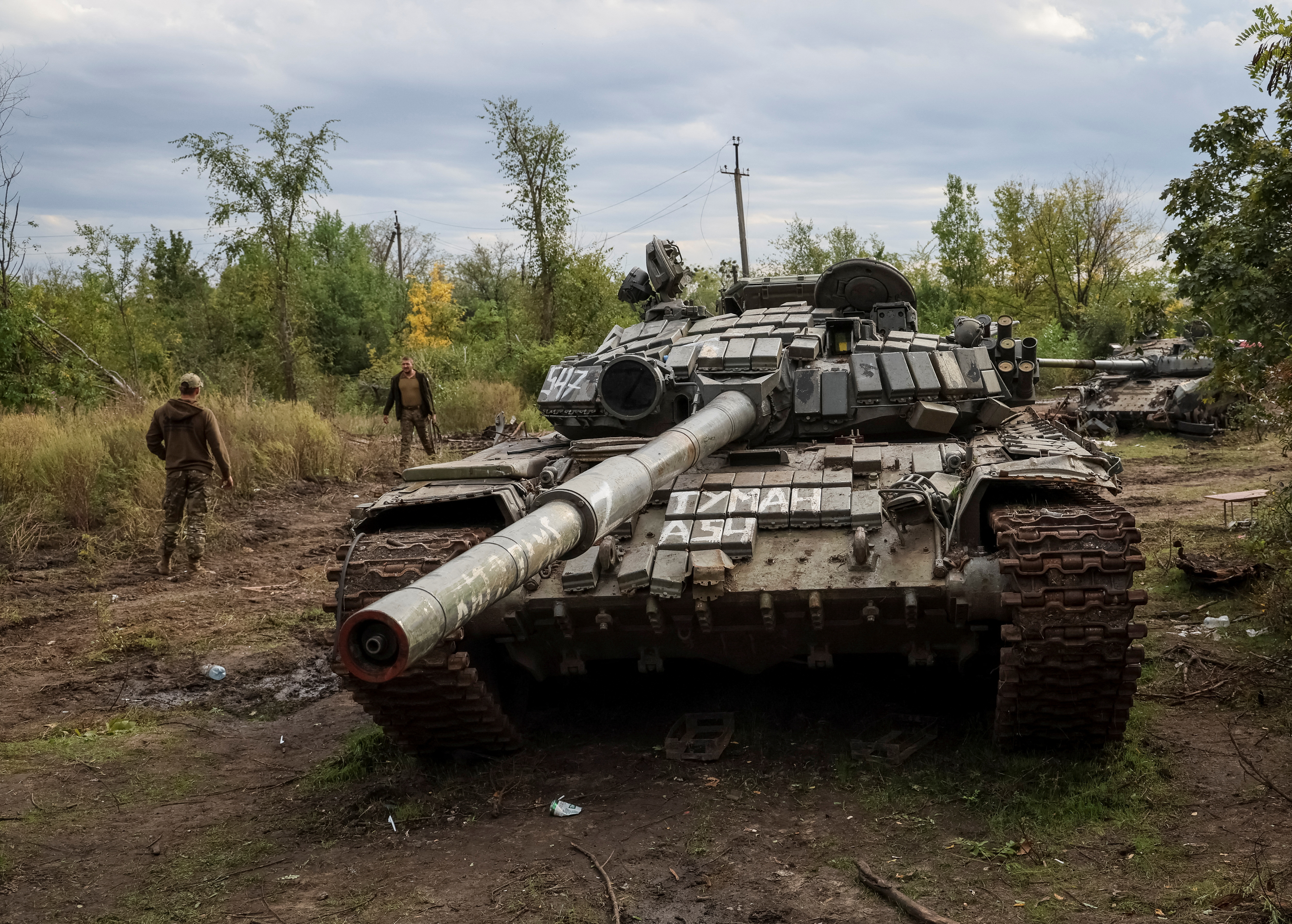 Ukrainian servicemen walk near destroyed Russian tanks in the town of Izium