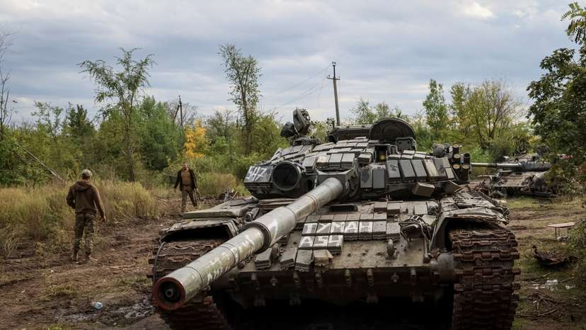 Ukrainian servicemen walk near destroyed Russian tanks in the town of Izium