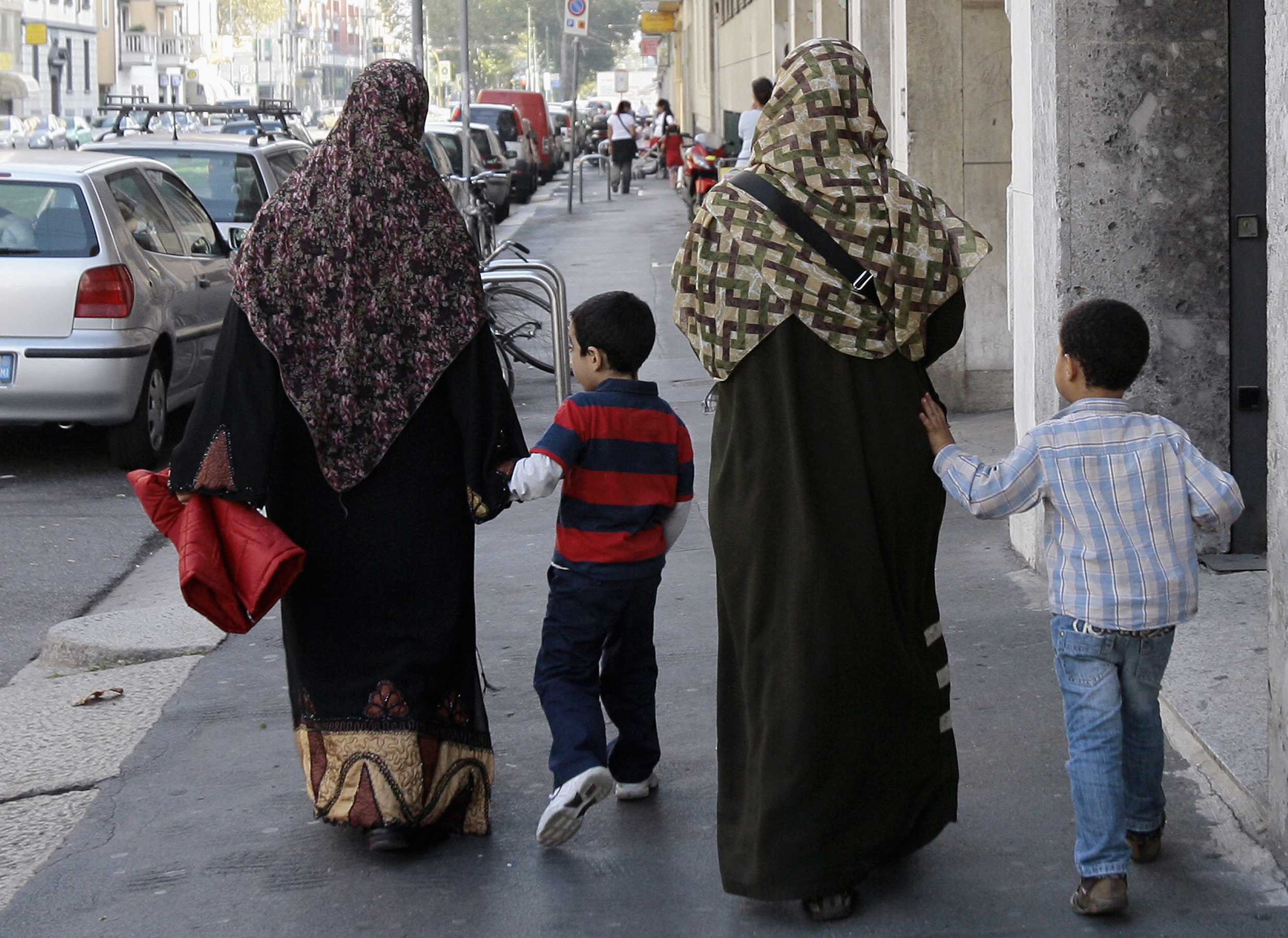 Two Muslim women wearing hijabs walk with children in Milan