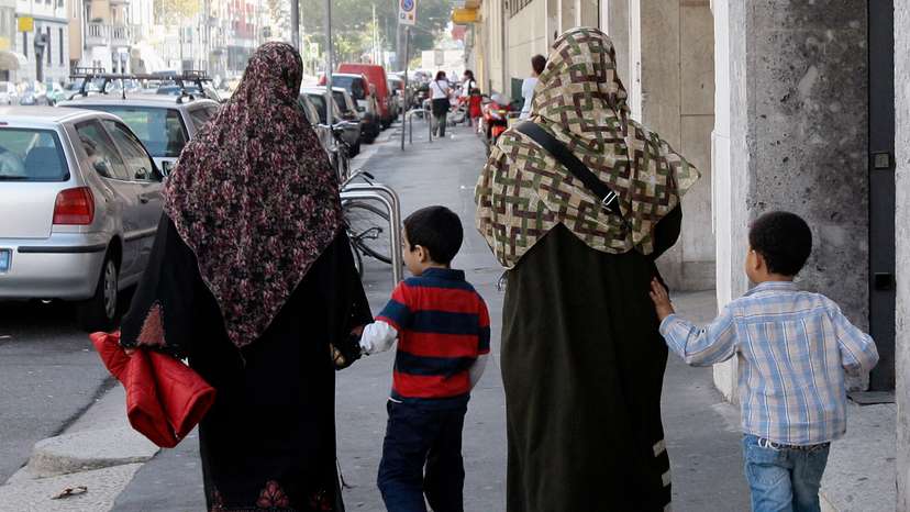 Two Muslim women wearing hijabs walk with children in Milan
