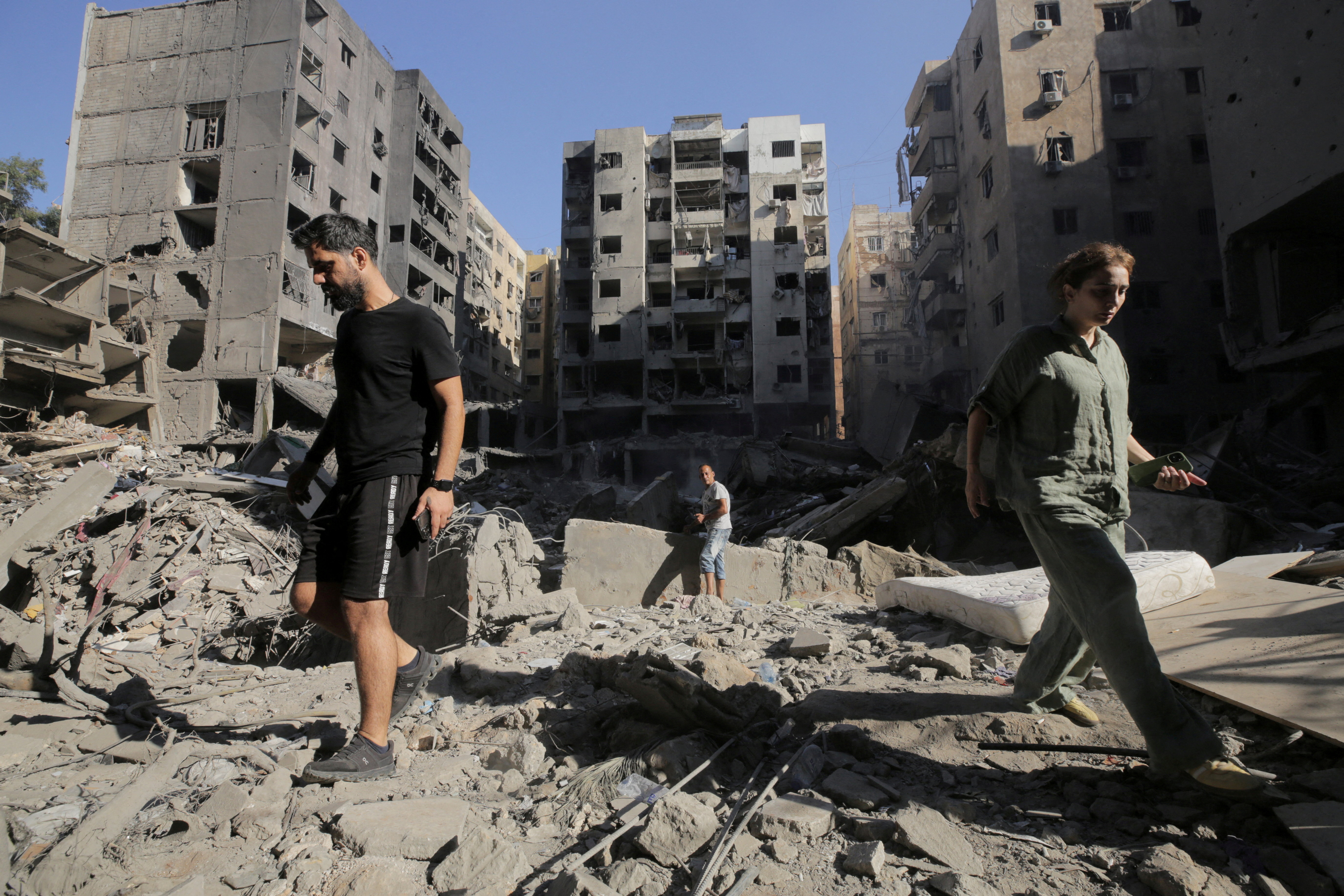 People walk on the rubble at the site of the Israeli airstrike that killed Lebanon's Hezbollah leader Sayyed Hassan Nasrallah on Friday, in Beirut's southern suburbs