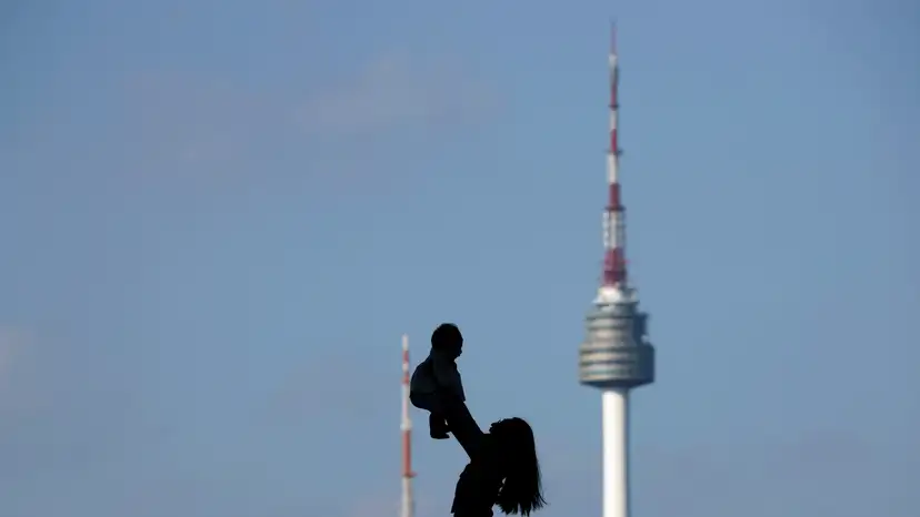 A woman holding up her baby is silhouetted against the backdrop of N Seoul Tower in Seoul