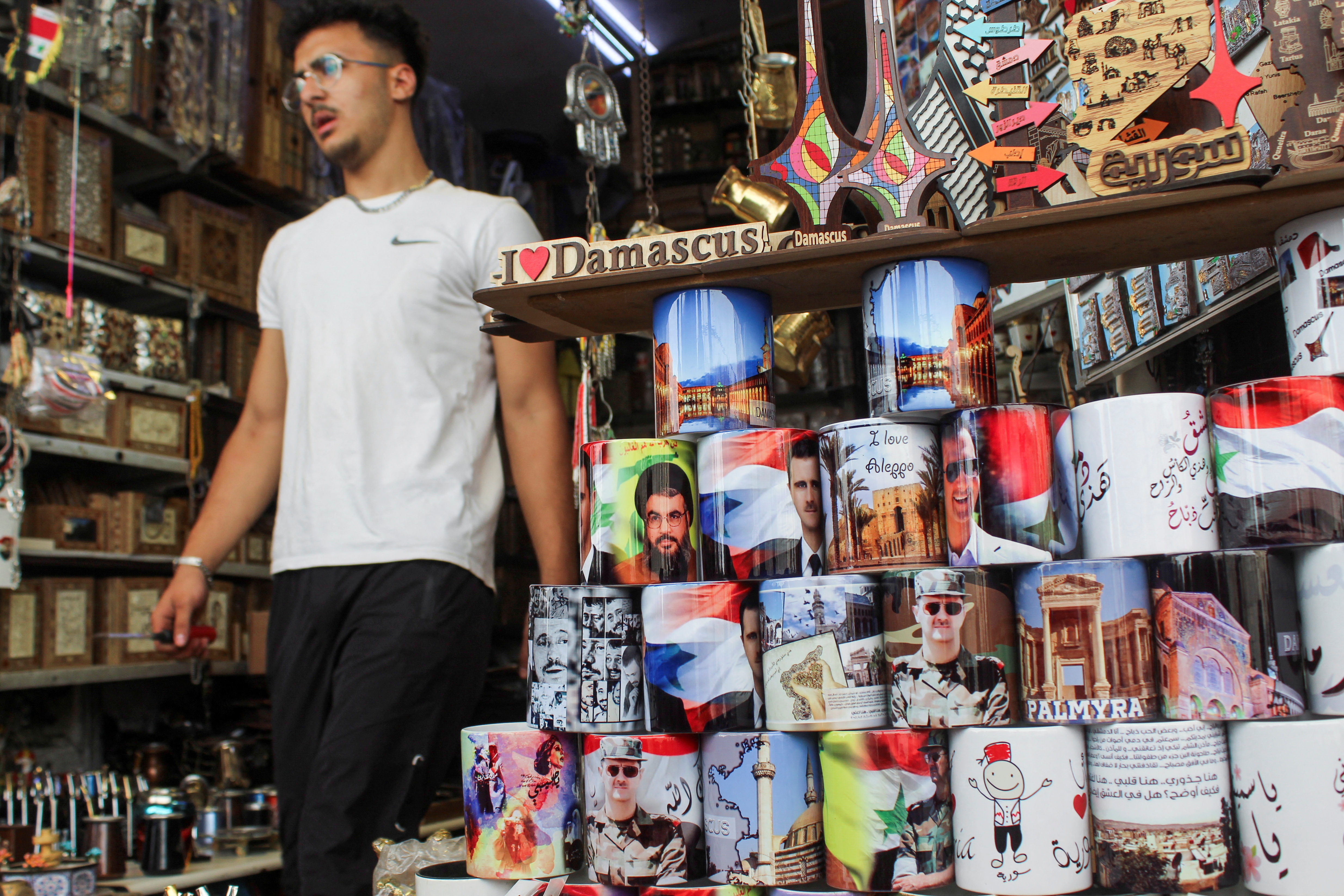 A man walks past mugs featuring  pictures of Syrian President Bashar al-Assad and Lebanon's Hezbollah leader Sayyed Hassan Nasrallah, who was killed in an Israeli airstrike on Friday, at a souvenir shop during national mourning for Nasrallah, in Damascus