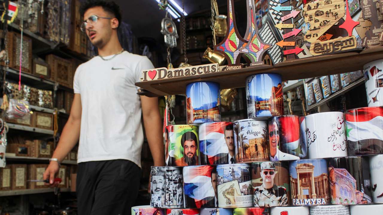 A man walks past mugs featuring pictures of Syrian President Bashar al-Assad and Lebanon's Hezbollah leader Sayyed Hassan Nasrallah, who was killed in an Israeli airstrike on Friday, at a souvenir shop during national mourning for Nasrallah, in Damascus
