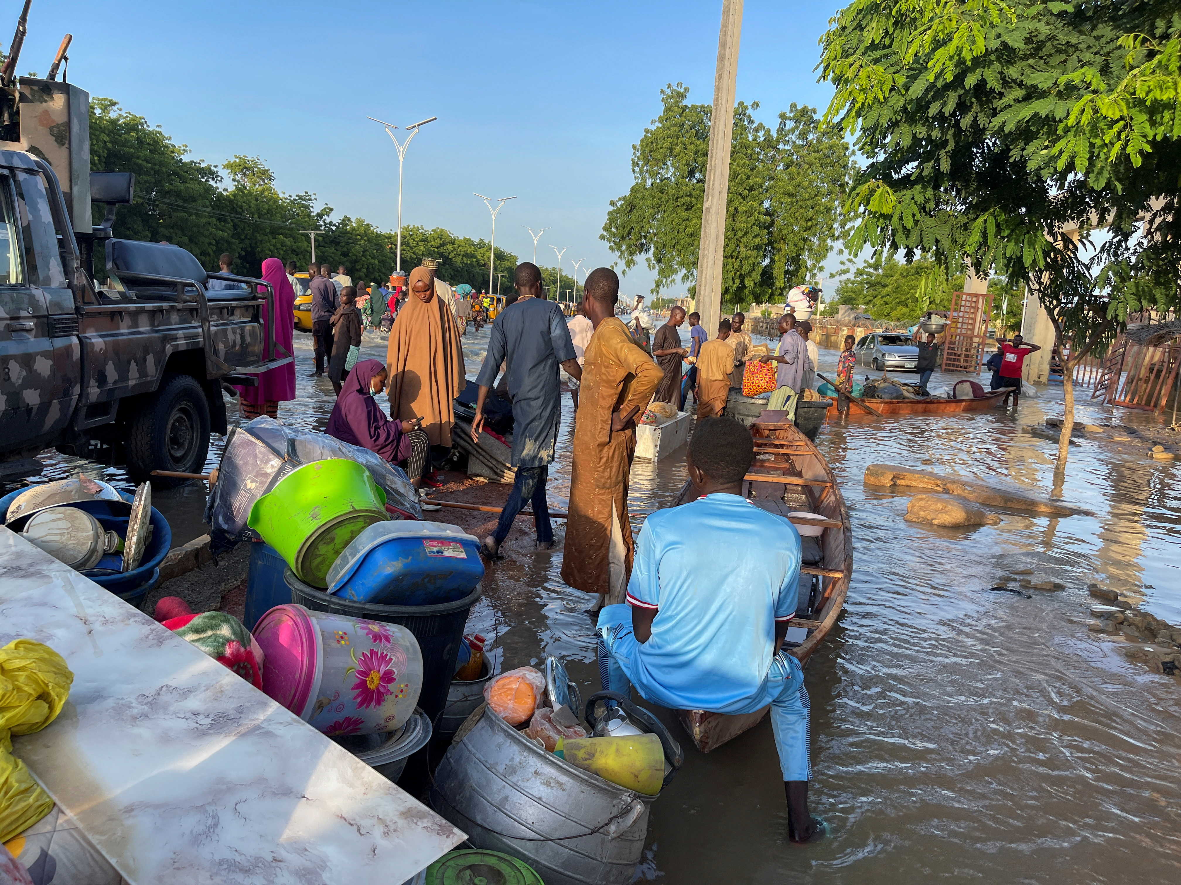 Flood victims stand beside their belongings offloaded from the canoe that helped them to move to safety in Maiduguri