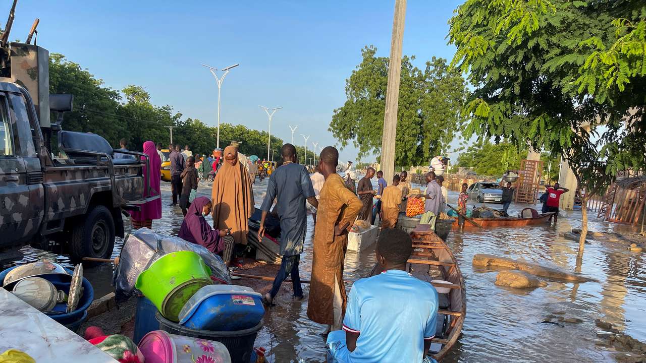 Flood victims stand beside their belongings offloaded from the canoe that helped them to move to safety in Maiduguri