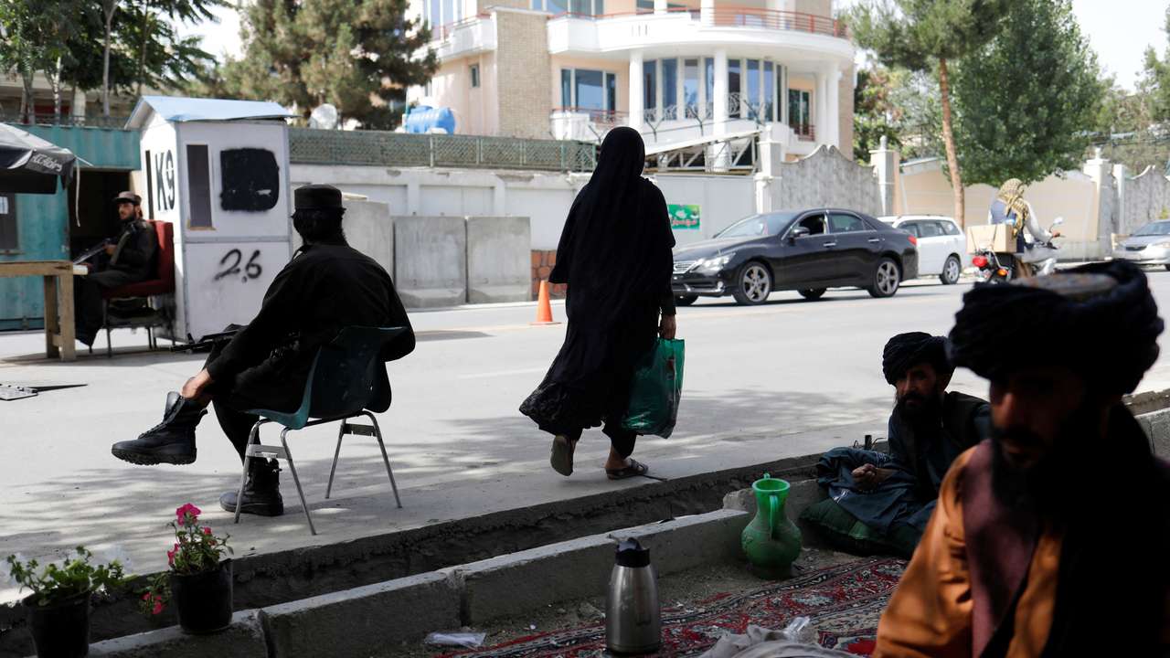 An Afghan woman walks among Taliban soldiers at a checkpoint in Kabul