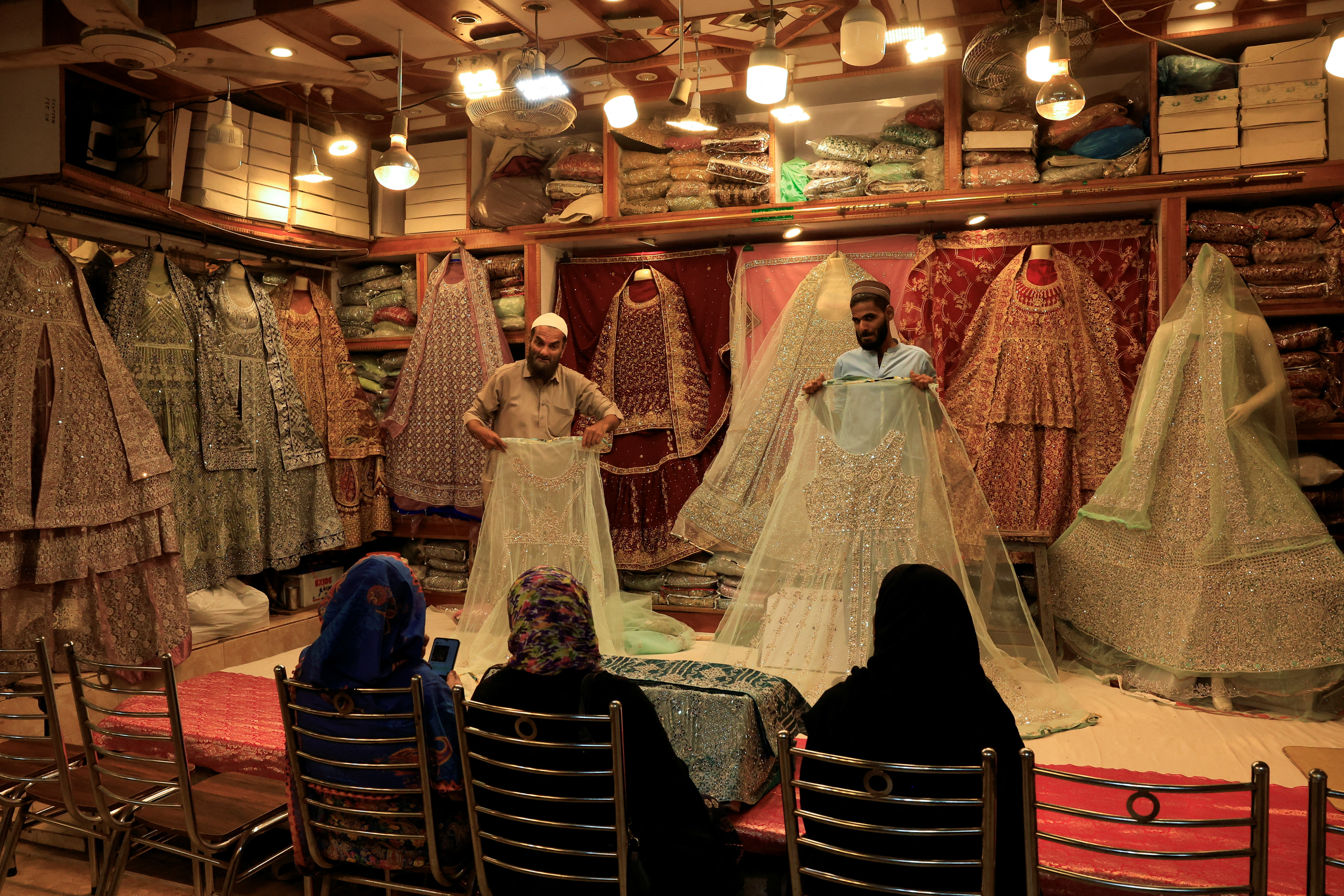 Shopkeepers display bridal dresses to customers at a shop in cloth market in Karachi