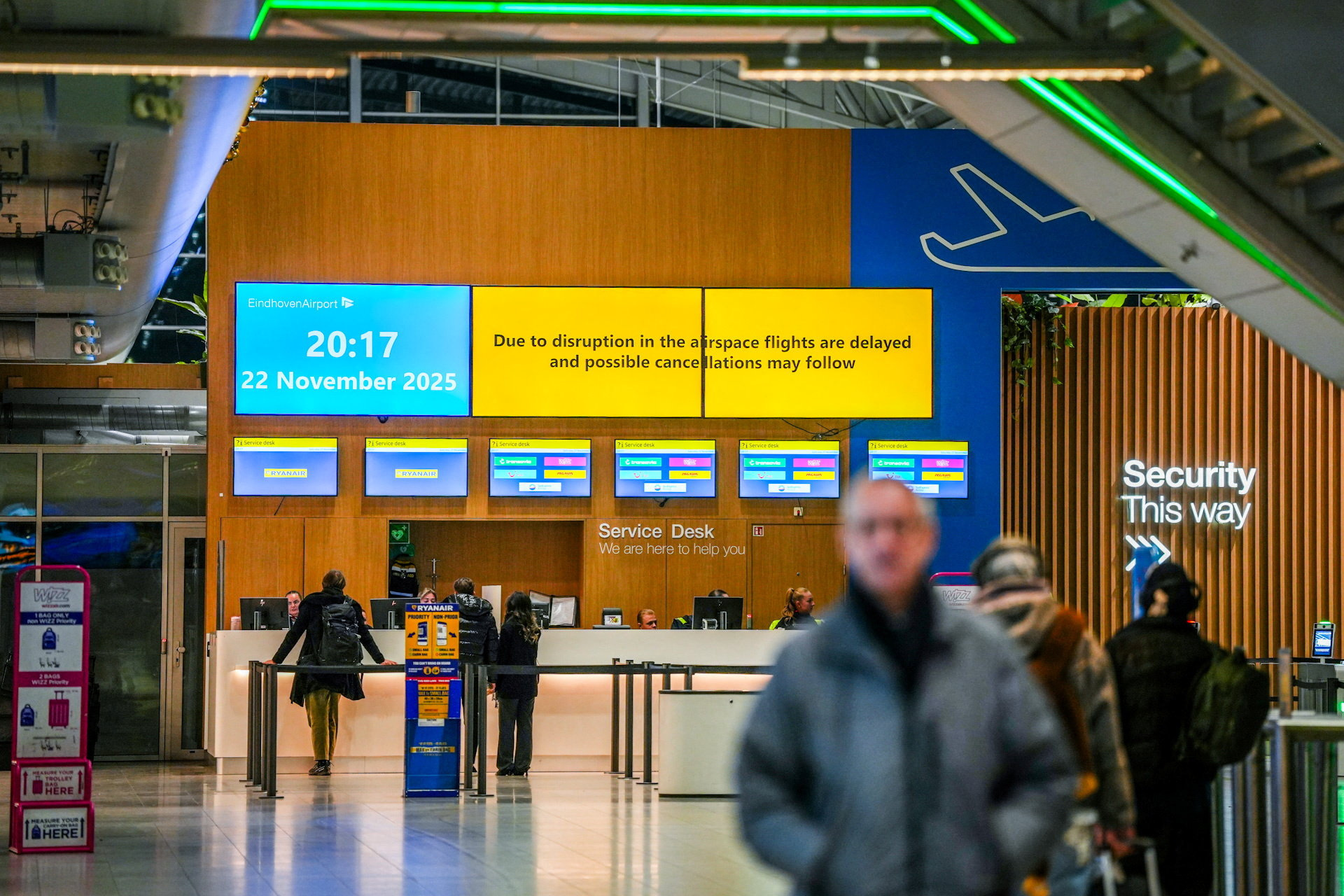 People stand at a service desk at Eindhoven Airport, as screens show a message about flight disruption, in Eindhoven