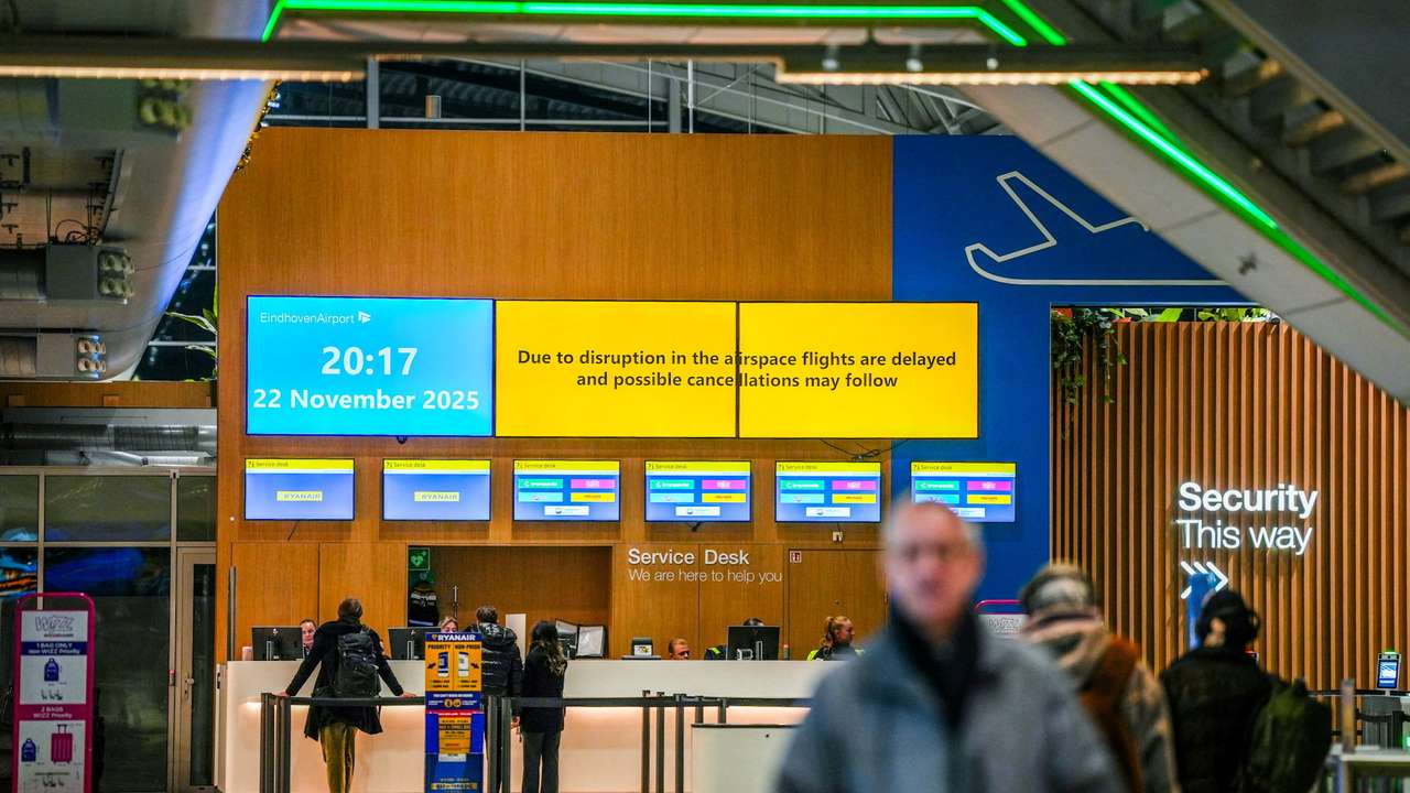 People stand at a service desk at Eindhoven Airport, as screens show a message about flight disruption, in Eindhoven