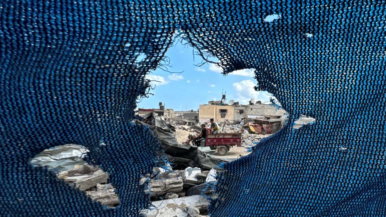 Palestinians, seen through a torn tent, ride a motorized vehicle past the rubble, amid the Israel-Hamas conflict, in Khan Younis, in the southern Gaza Strip