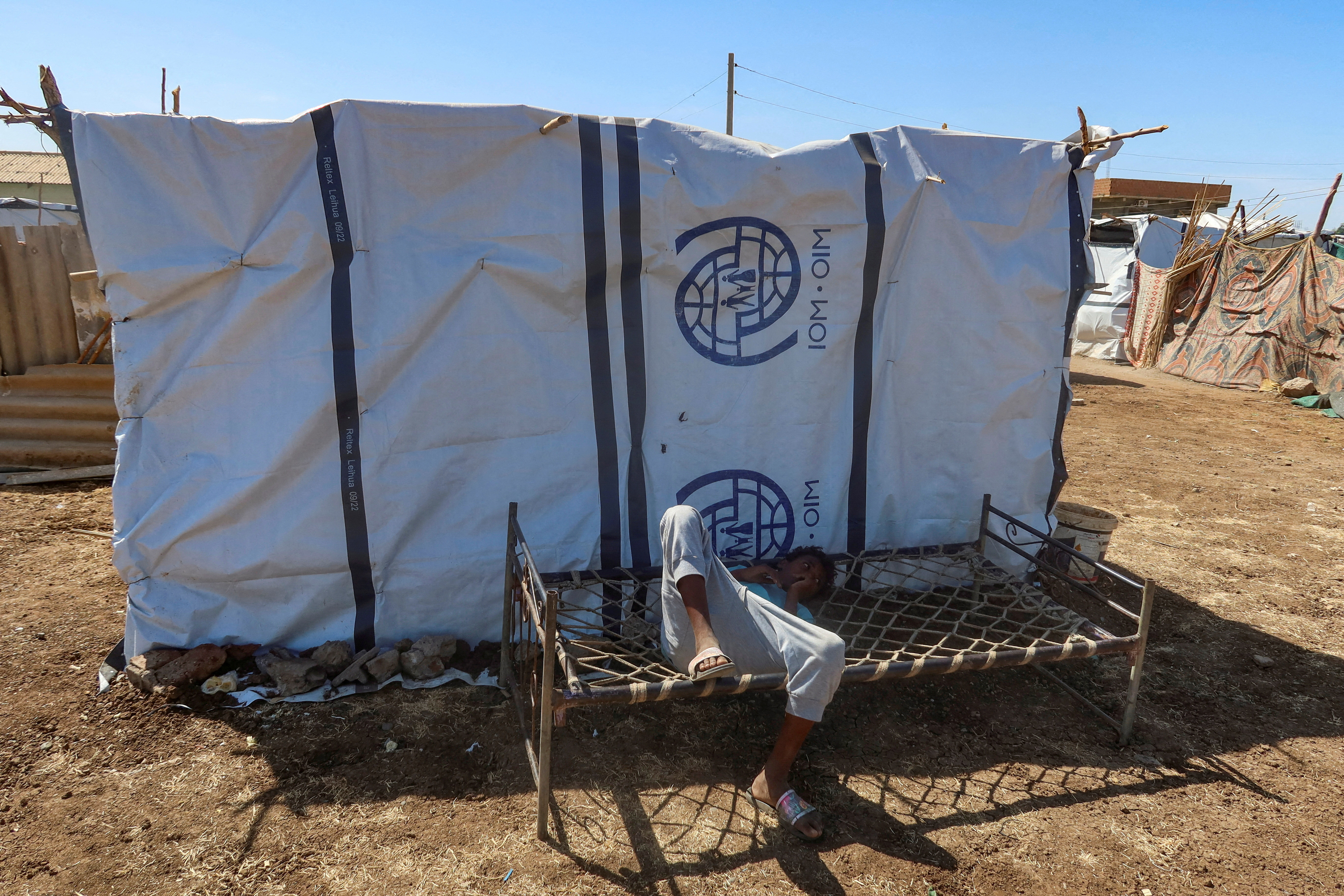 FILE PHOTO: A boy displaced from Sudan's Gezira state lies down on a bench with the logo of the International Organization for Migration New Halfa