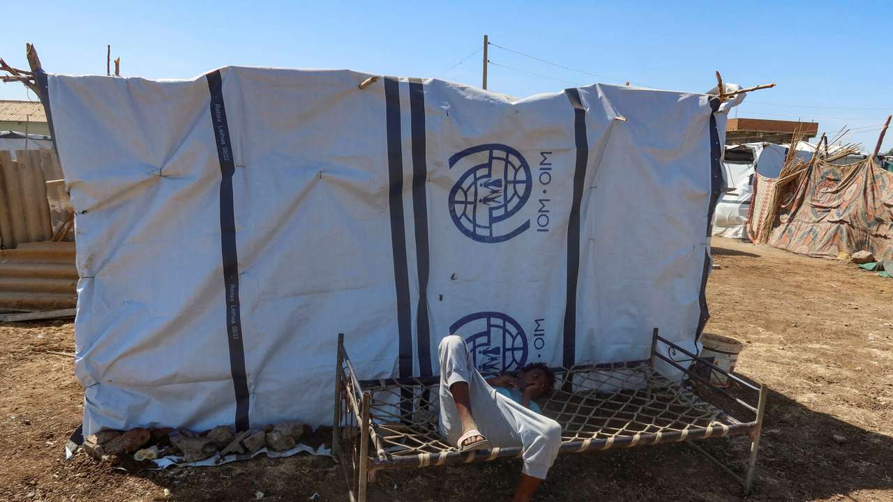 FILE PHOTO: A boy displaced from Sudan's Gezira state lies down on a bench with the logo of the International Organization for Migration New Halfa