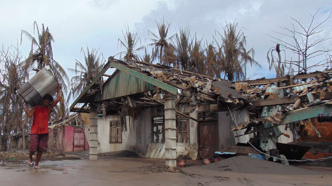 A person carries his belongings as he walks past a damaged house affected by the eruption of Mount Ruang volcano in Laingpatehi village