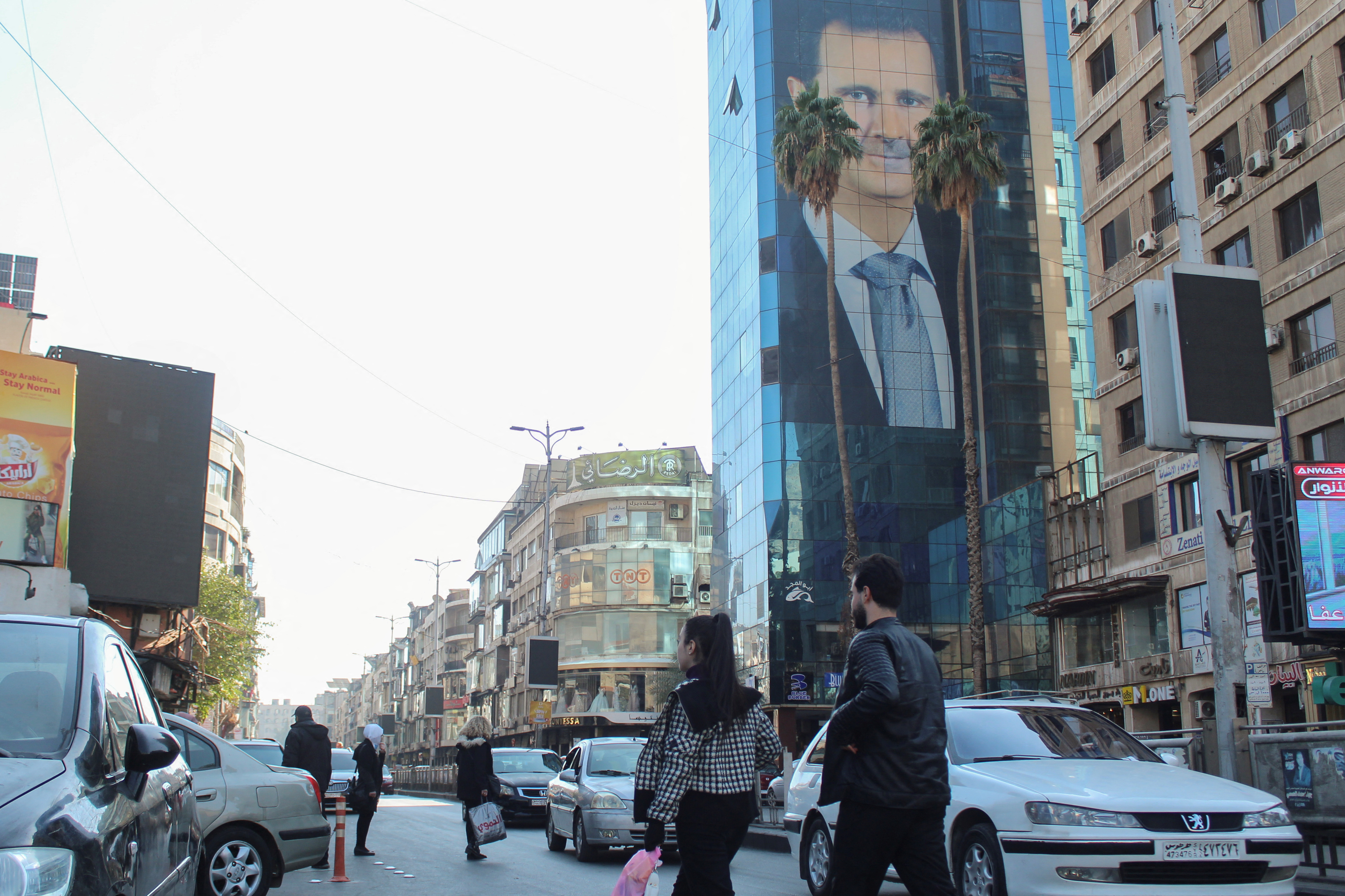 People walk near a poster depicting Syria's President Bashar al-Assad in Damascus