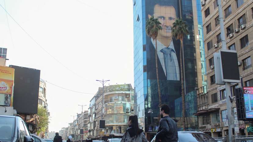 People walk near a poster depicting Syria's President Bashar al-Assad in Damascus