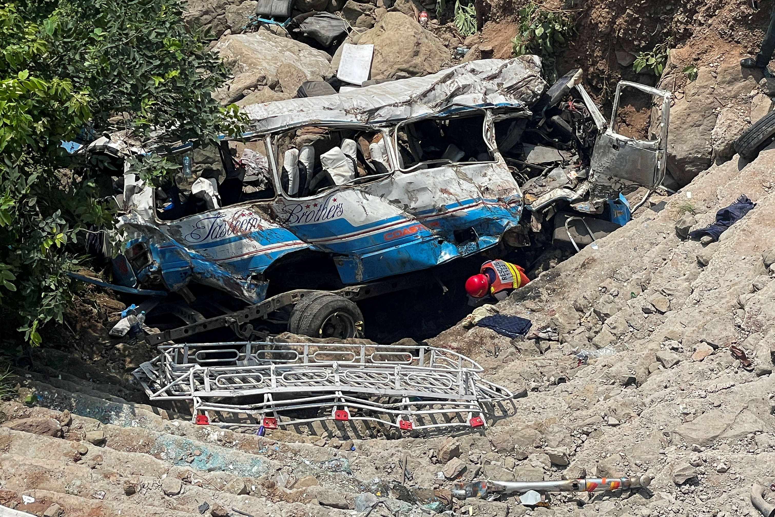 Rescue worker operates on the site of a damaged passenger bus, after it plunged into a deep ravine in Kahuta