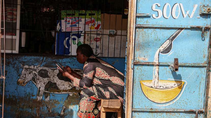 FILE PHOTO: A woman uses her mobile phone as she waits for a customer at her family shop in Bargny, on the outskirts of Dakar