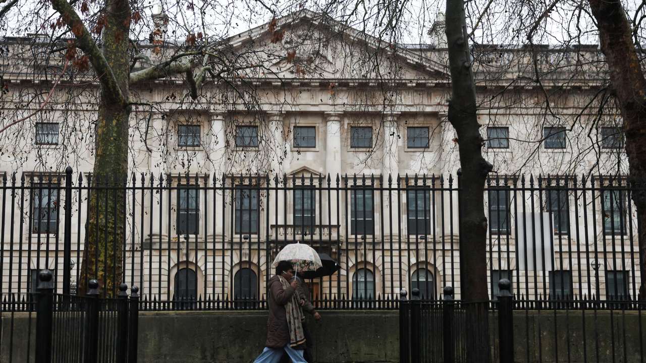 People shelter under umbrellas as they walk past the Royal Mint Court, the proposed site of the new Chinese embassy, in London