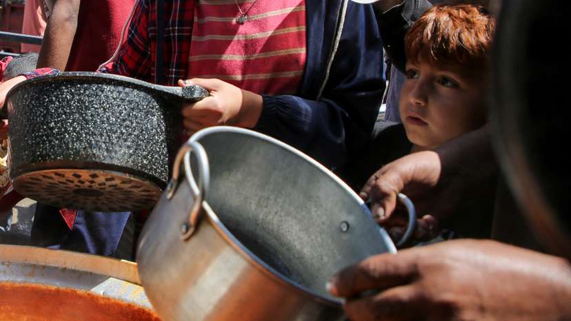 Palestinians wait to receive food cooked by a charity kitchen, in Rafah, in the southern Gaza Strip
