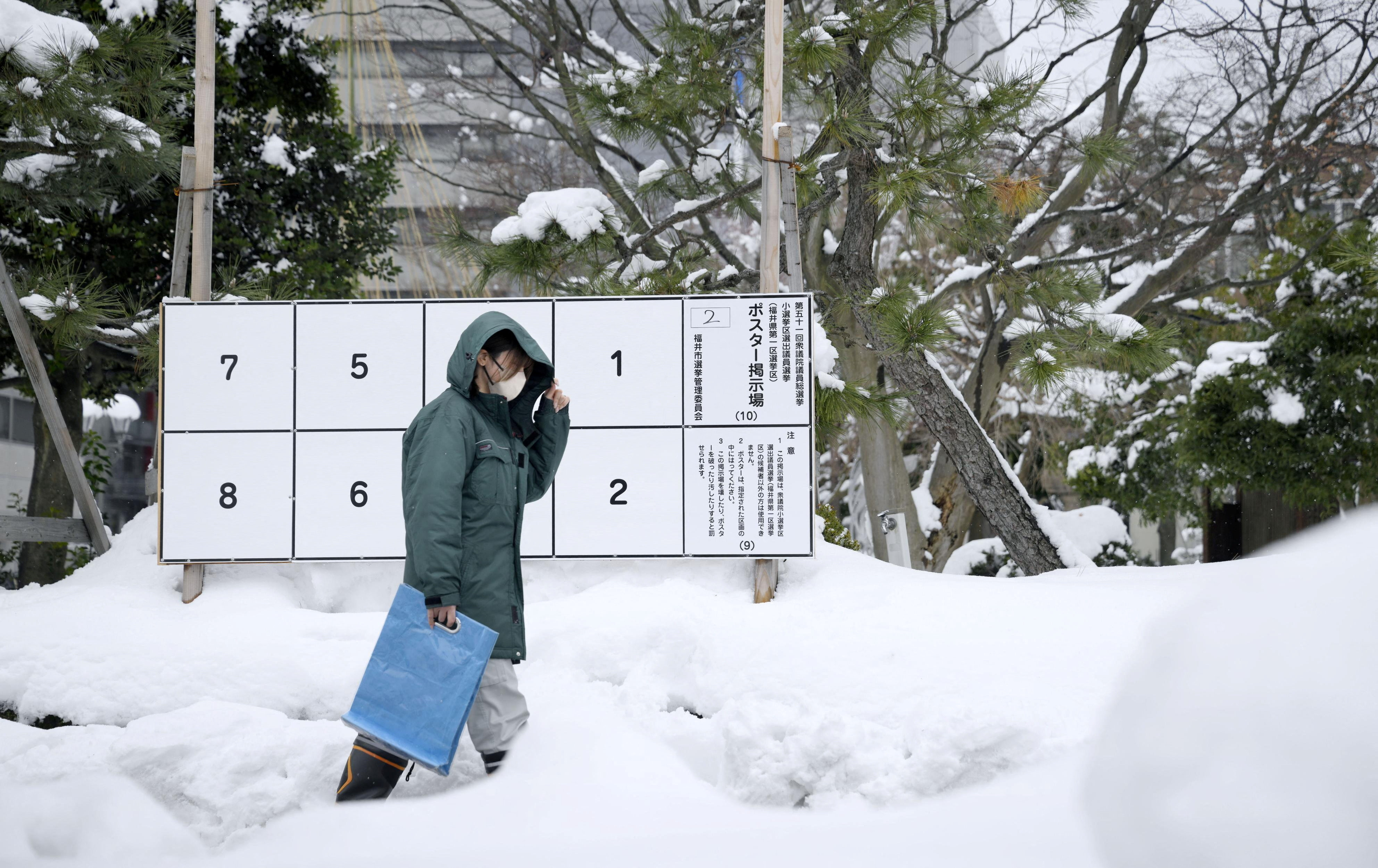 A person walks past a bulletin board for posters of candidates for the February 8 snap election, where snow has accumulated, in Fukui