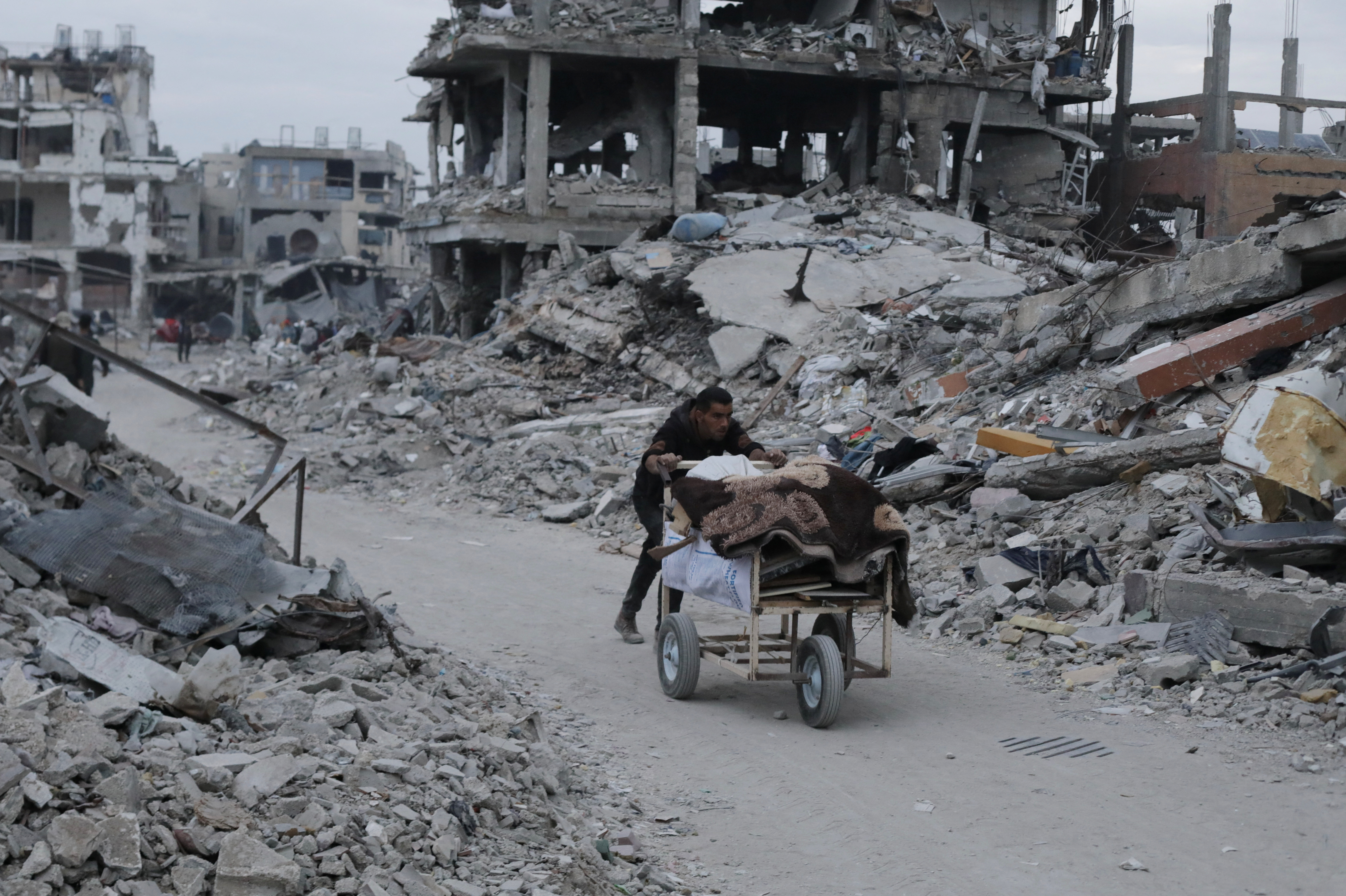Palestinian pushes belongings past the rubble of buildings and houses destroyed during the Israeli offensive, amid a ceasefire between Israel and Hamas, in Jabalia