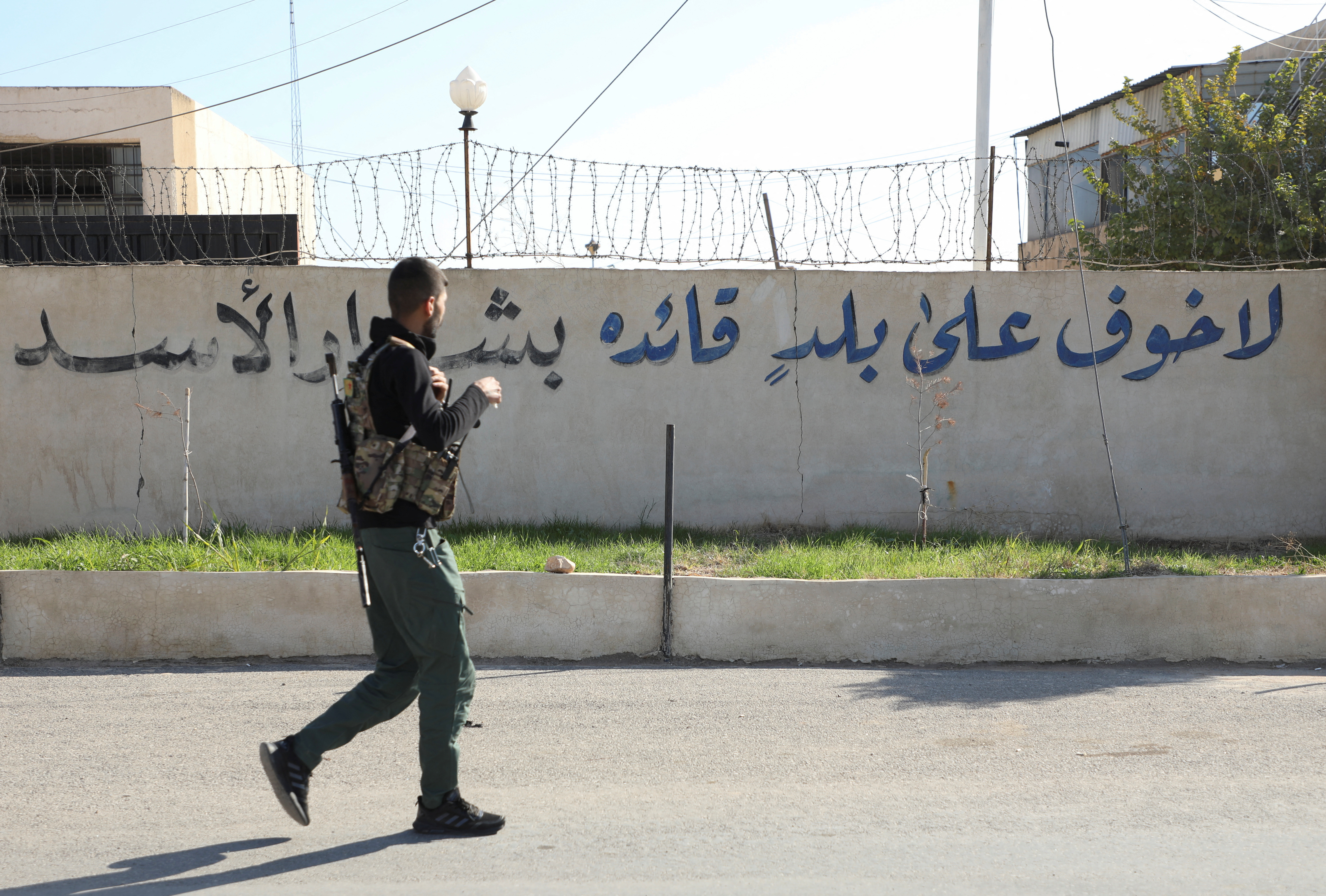 SDF member walks near a writing on a wall in Qamishli
