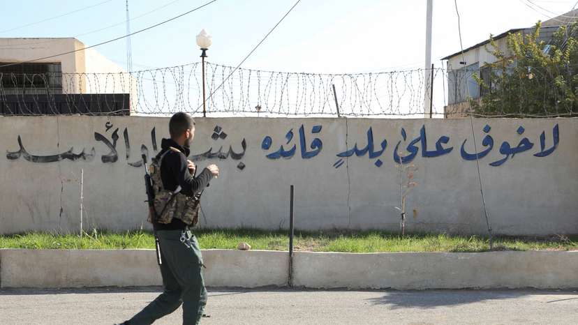 SDF member walks near a writing on a wall in Qamishli