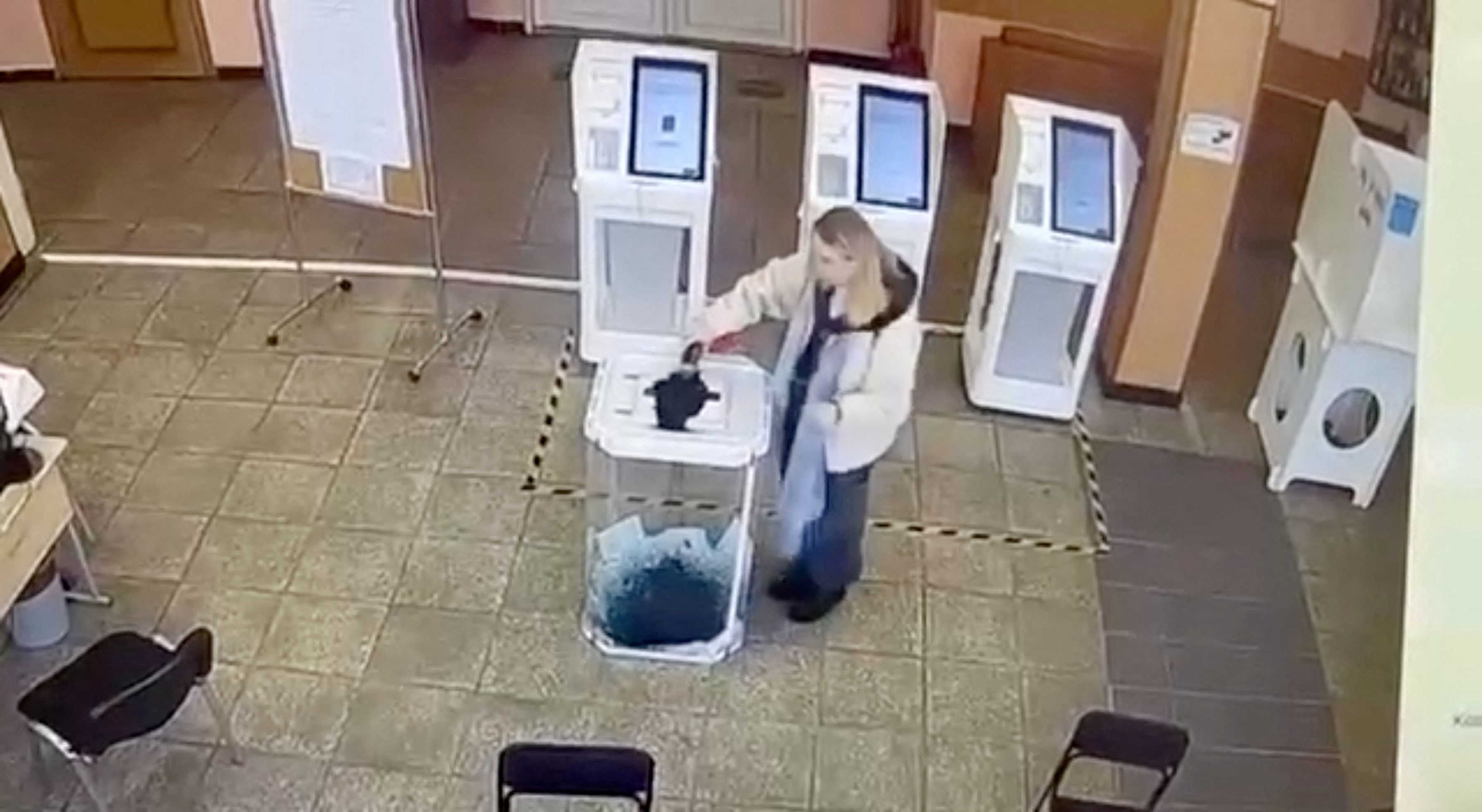 A woman pours a liquid into a ballot box,  during the Russian presidential election in Moscow