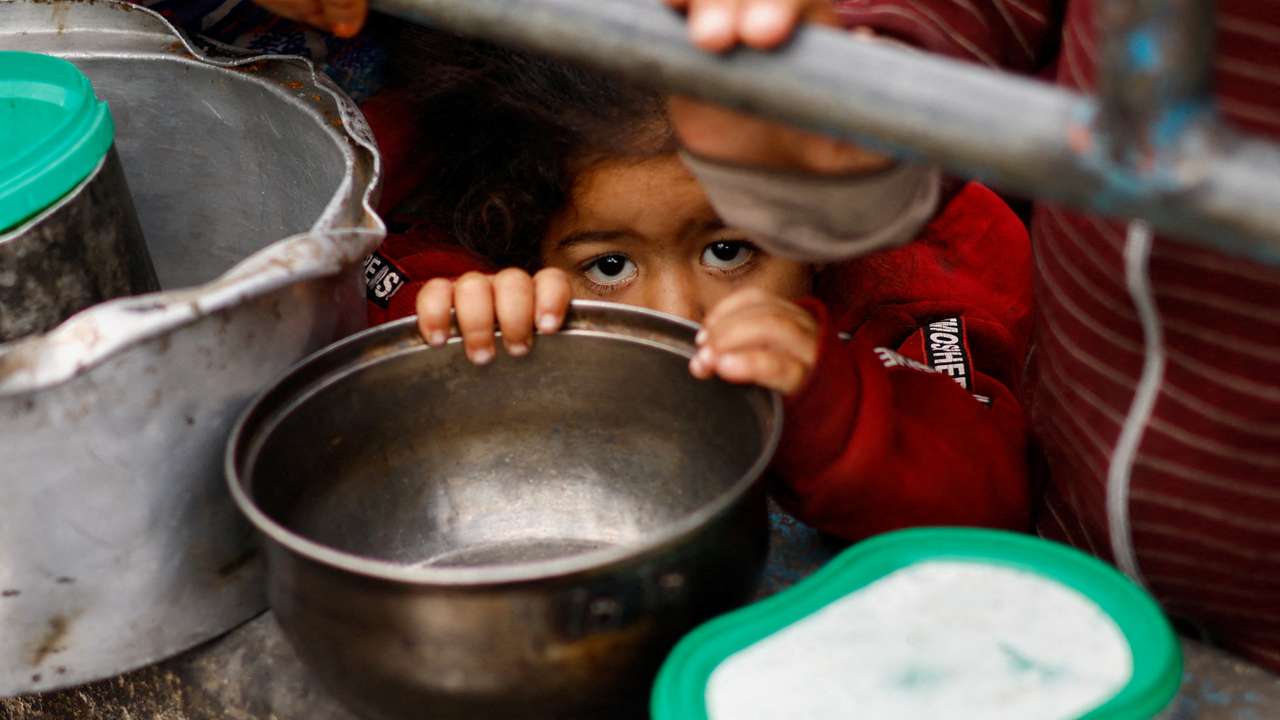 Palestinian children wait to receive food cooked by a charity kitchen amid shortages of food supplies, in Rafah