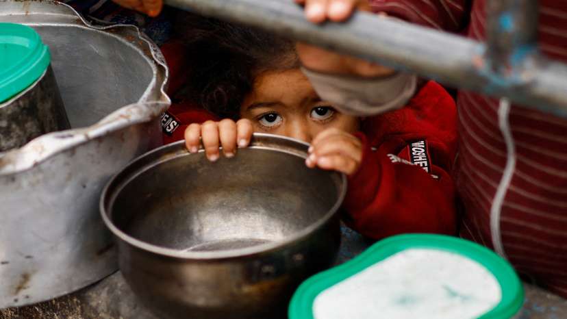 Palestinian children wait to receive food cooked by a charity kitchen amid shortages of food supplies, in Rafah