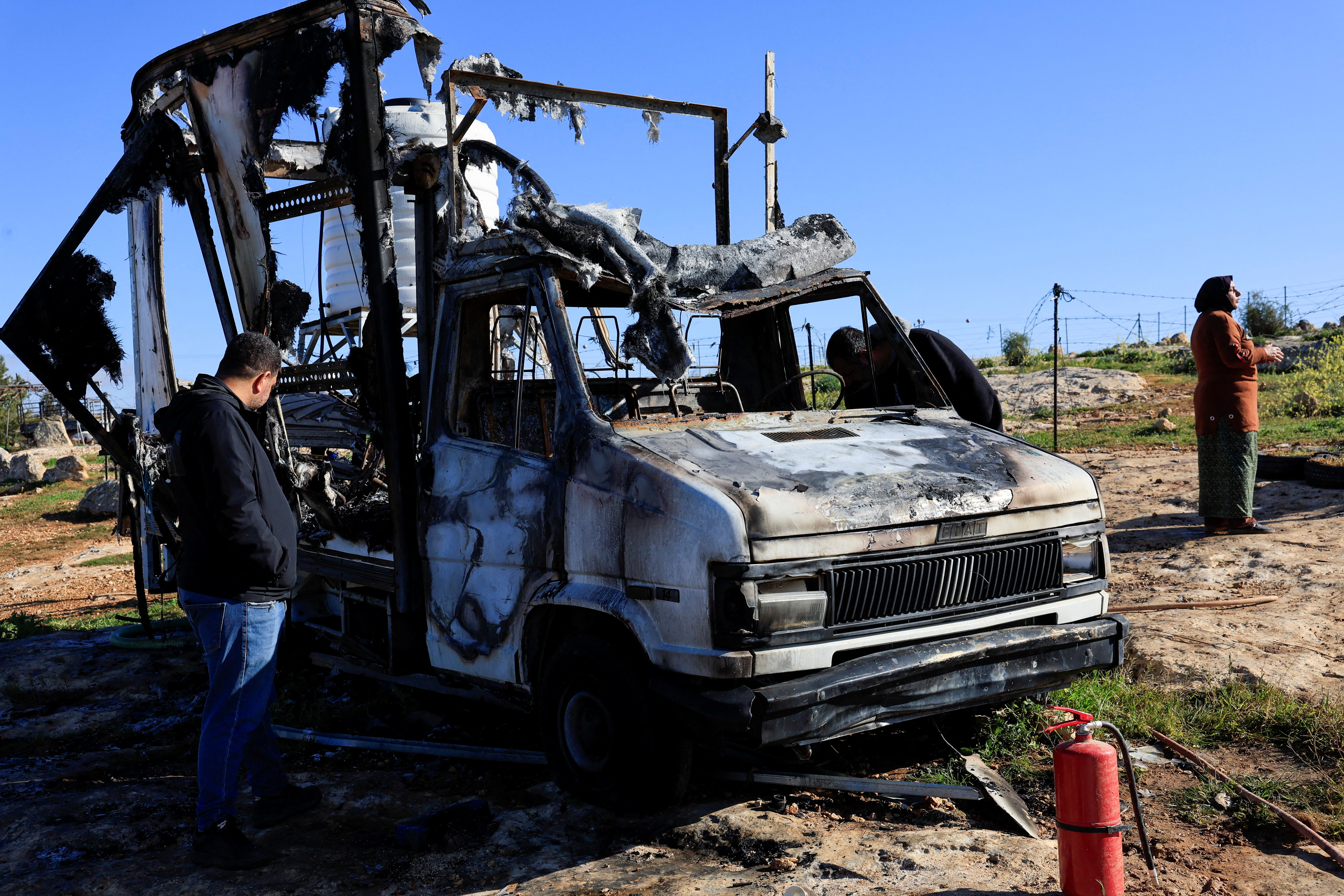 Palestinians check damage to a burned vehicle, in Susiya near Hebron