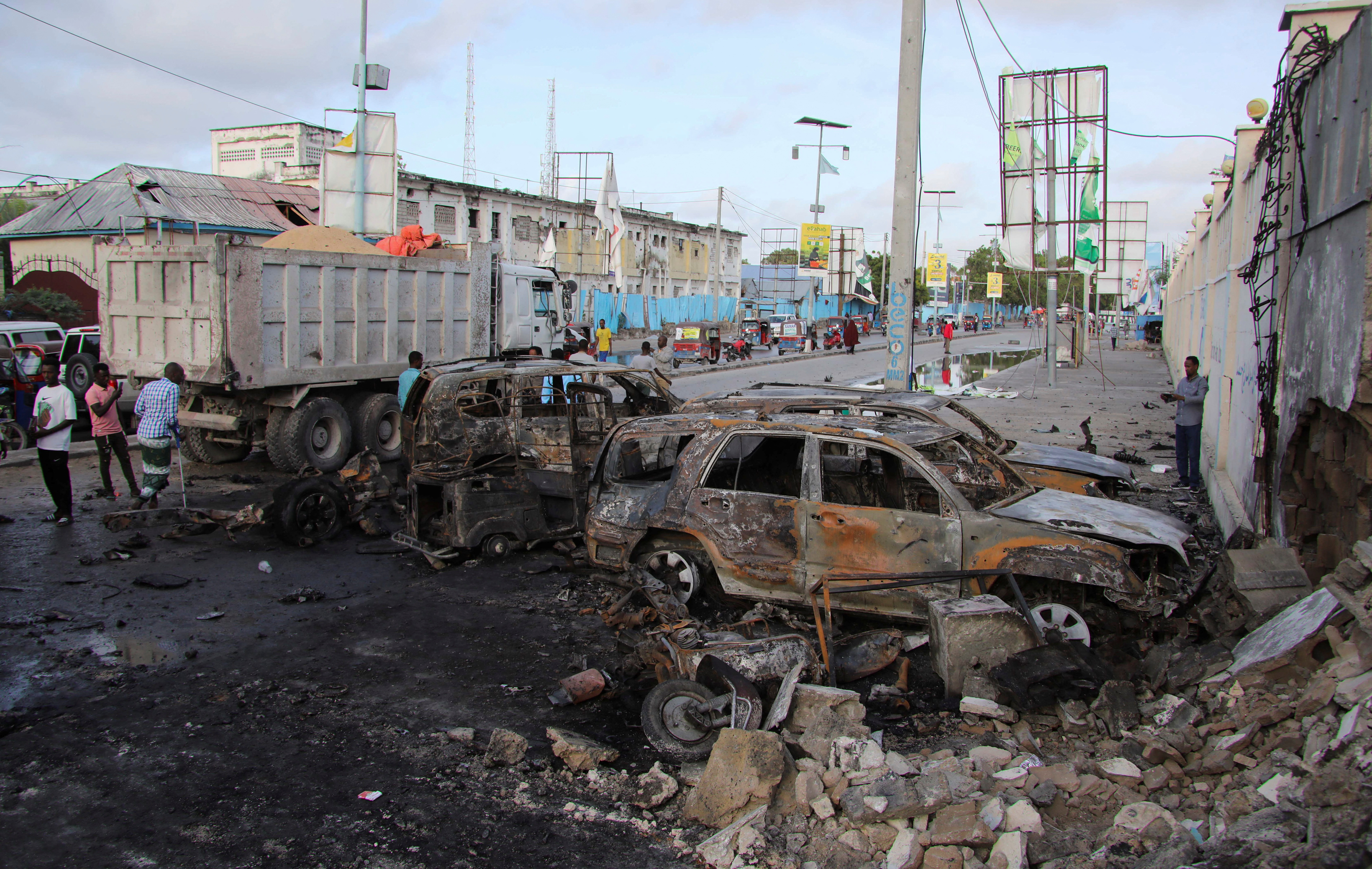 People gather near the wreckages of vehicles destroyed at the scene of an explosion outside a restaurant were patrons were watching the final of the Euro 2024 football tournament on TV, in Bondhere district of Mogadishu