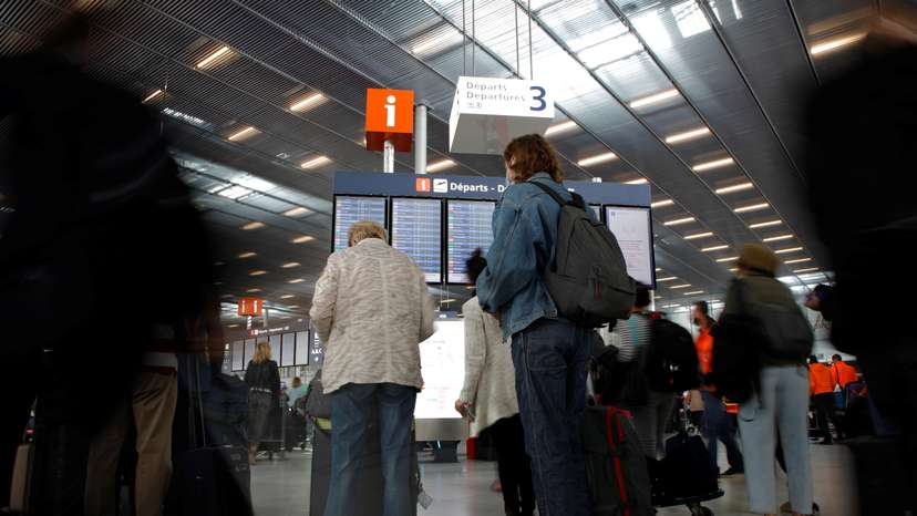 Passengers stand in front of a departures board at Orly Airport
